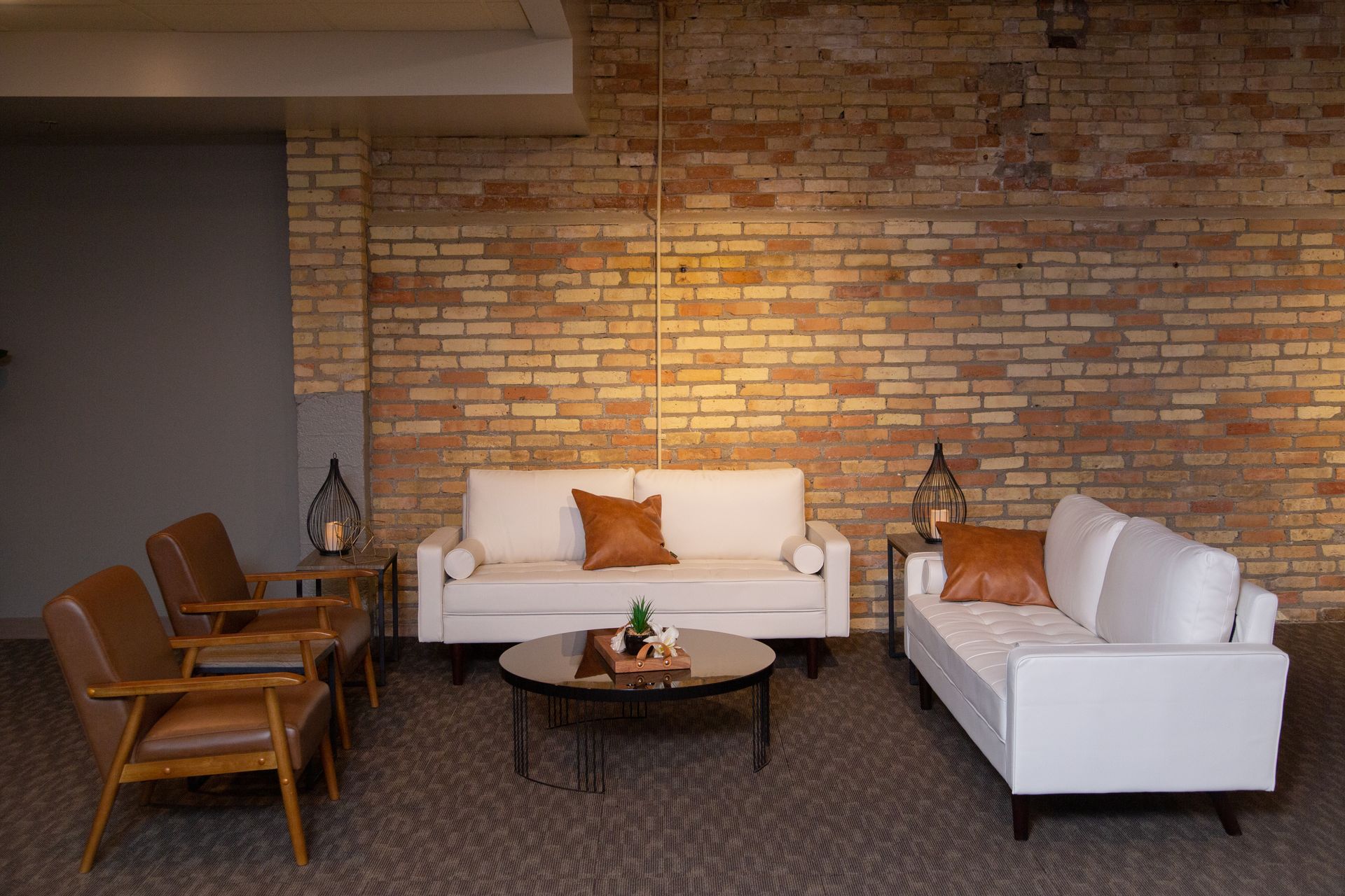 Cozy lounge with brick wall, white sofas, wooden chairs, and a round coffee table with plants.