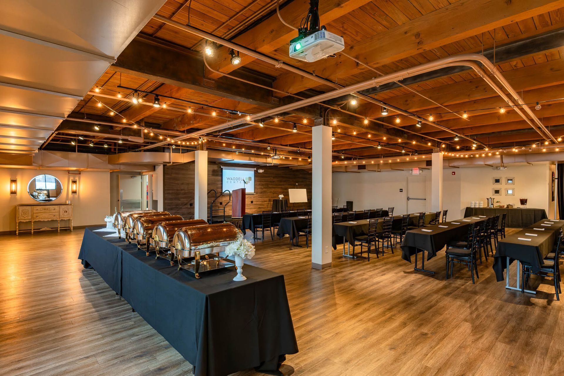 Spacious modern event hall with long tables, chairs, and a buffet setup under warm ceiling lights