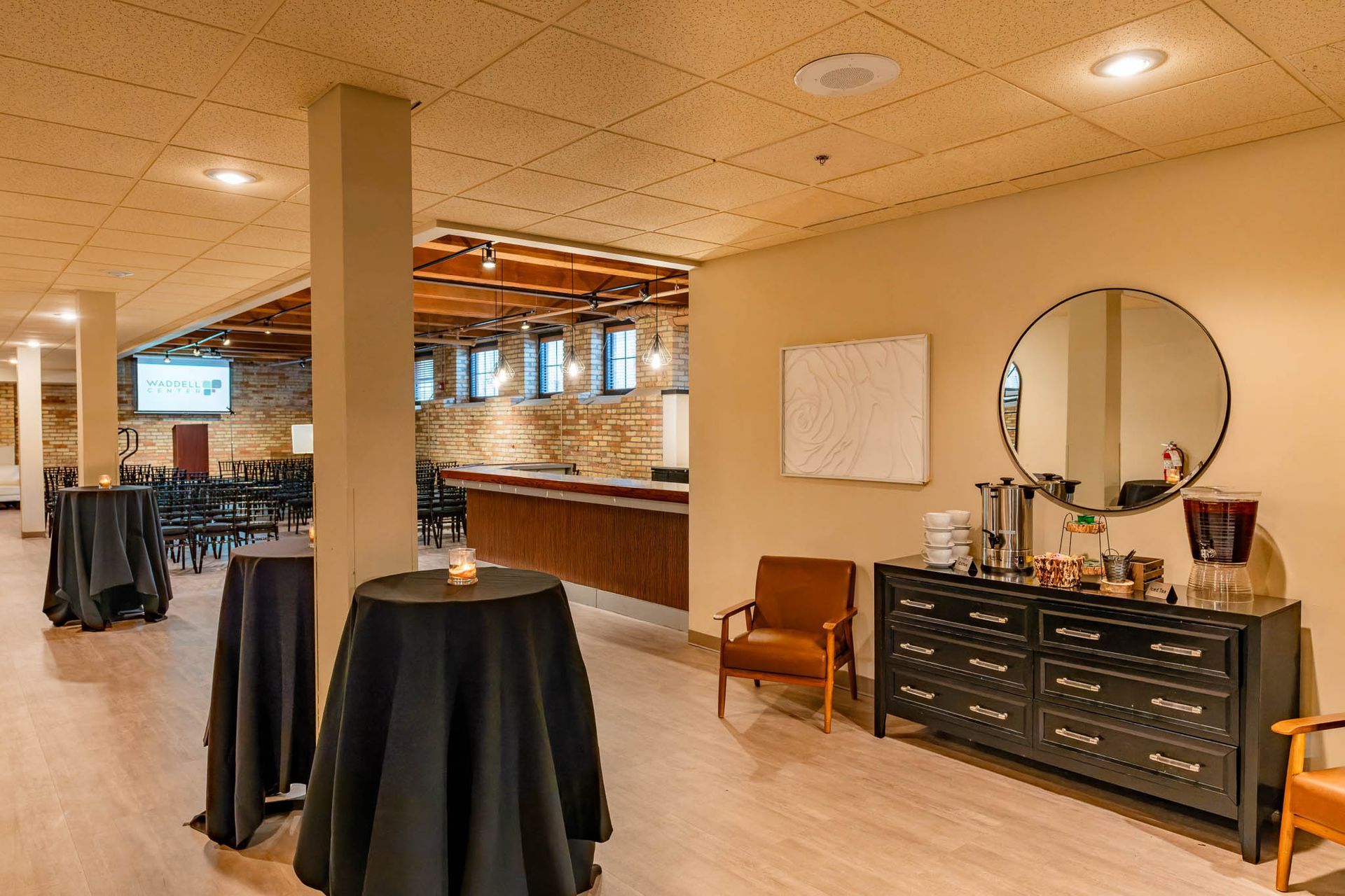 Elegant basement lounge with high-top tables, brick walls, bar counter, and a vanity dresser with mirror