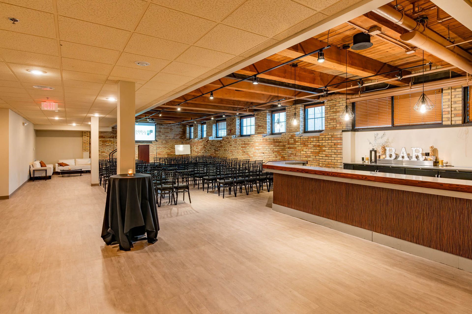 Empty modern event hall with exposed beams, rows of chairs, and a long wooden bar counter