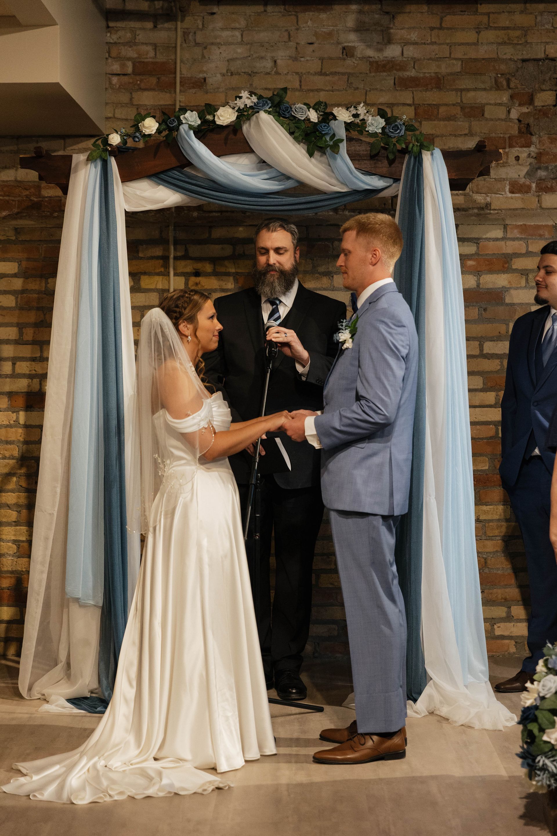 Bride and groom exchange vows under a floral arch during an indoor wedding ceremony.