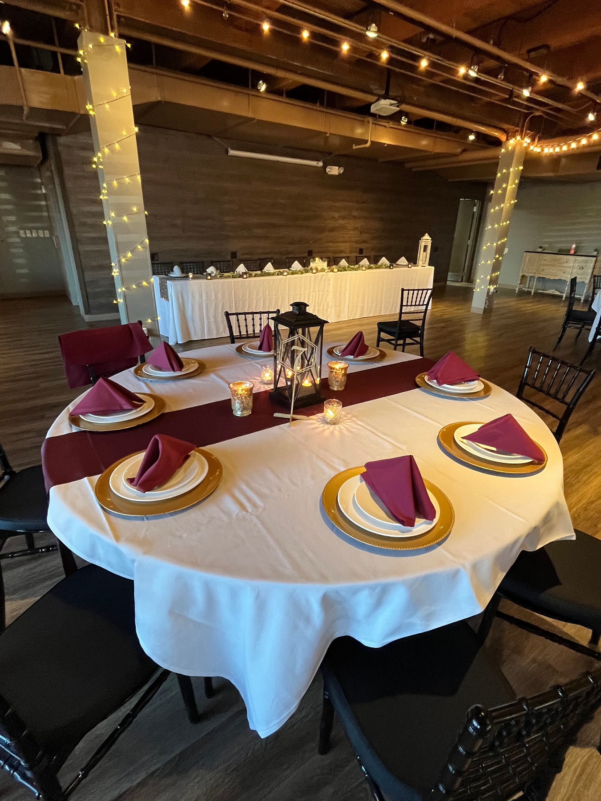 Round banquet table with burgundy and gold place settings in a rustic indoor event space