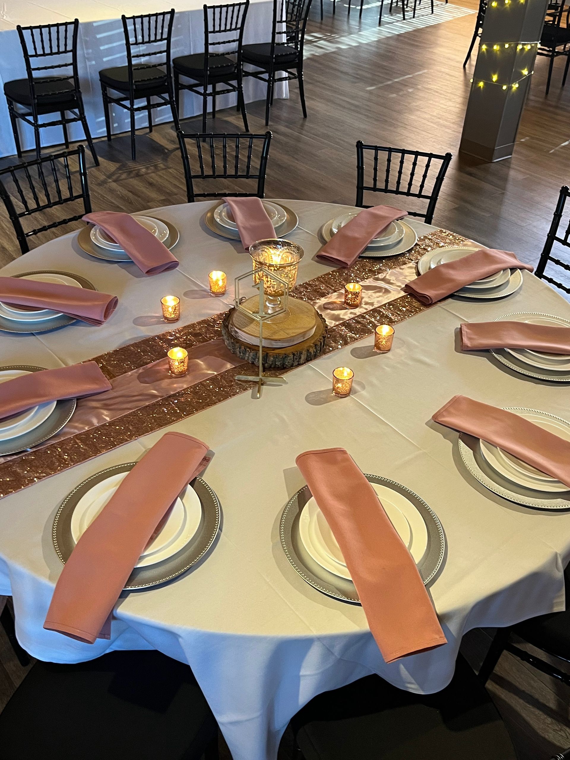 Round banquet table set with pink napkins, candles, and gold centerpiece in a dimly lit event hall