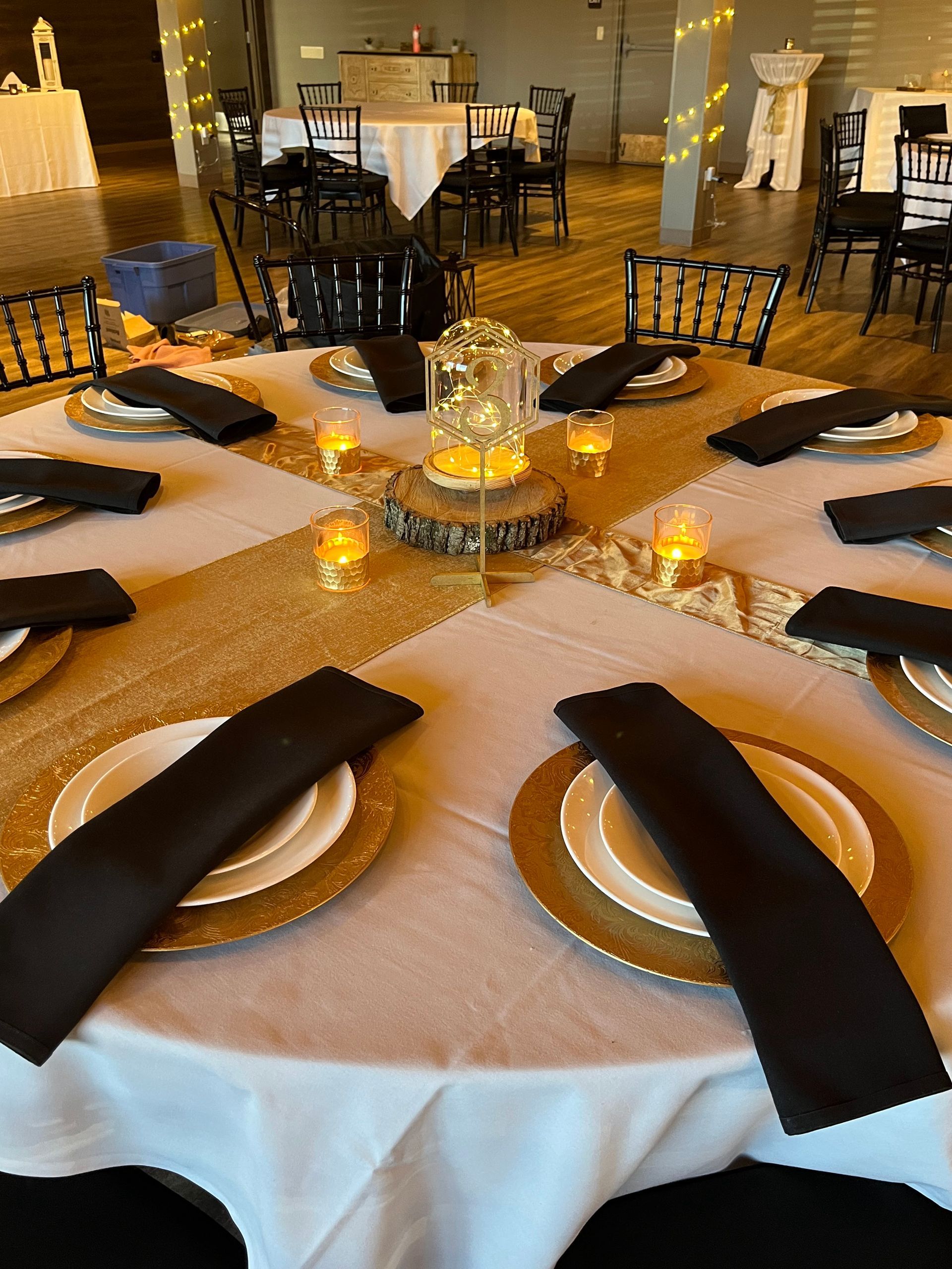Round banquet table set with black napkins, white plates, and lit candles in an elegant dining room