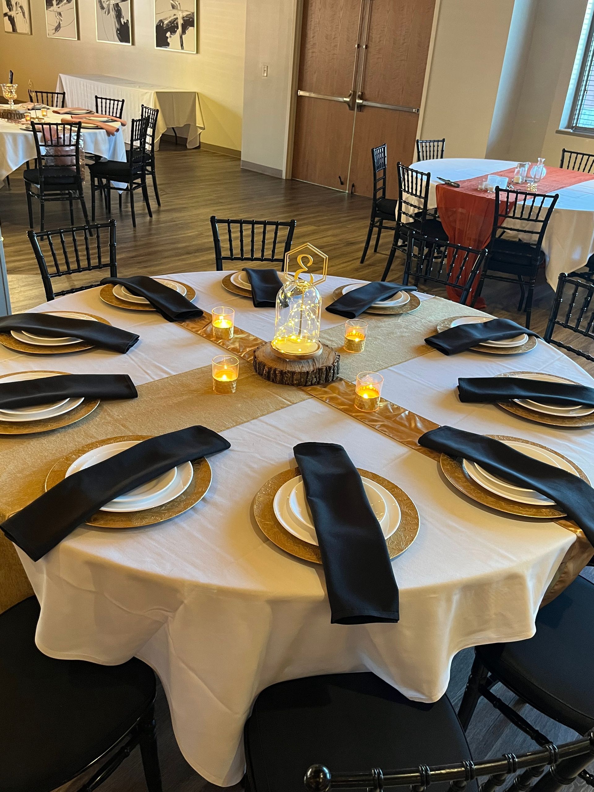 Banquet table with black napkins, gold charger plates, and candle centerpiece in a reception hall