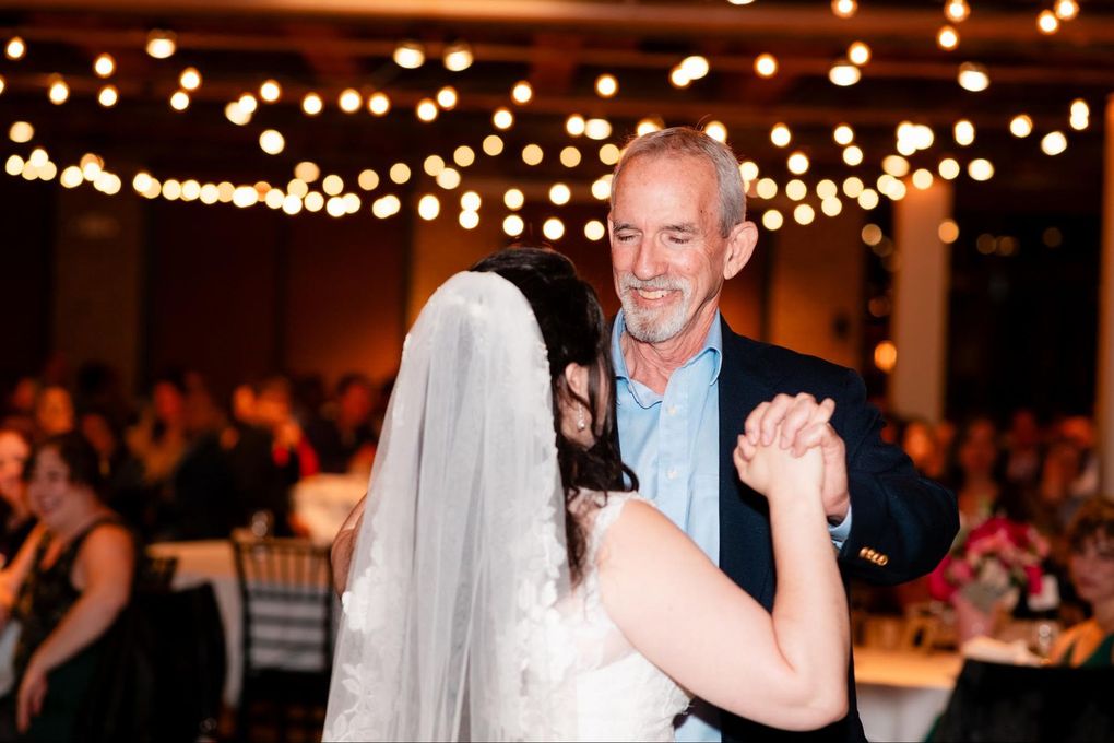 Bride and older man dancing at a reception under warm string lights