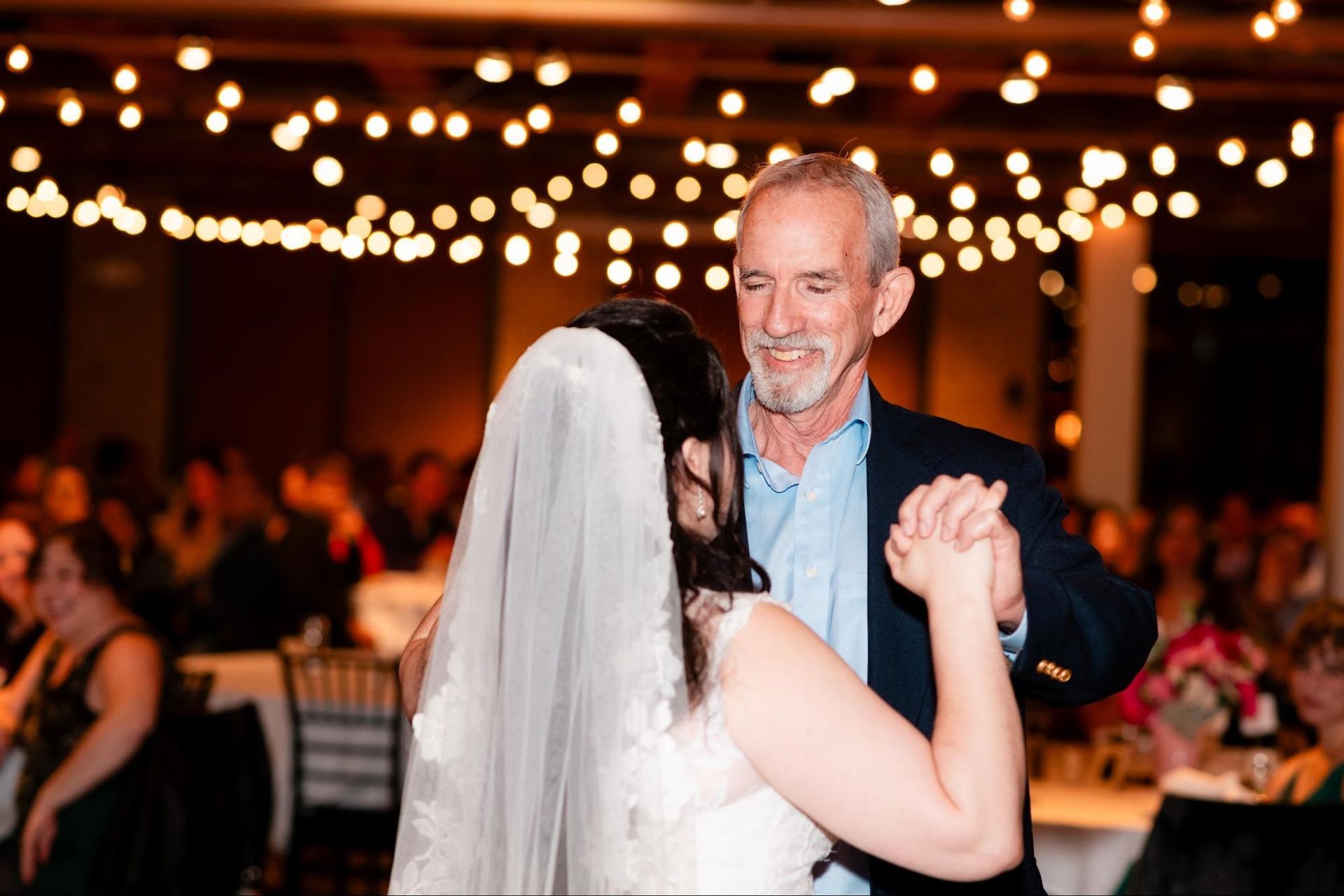 Bride and older man dancing at a reception under warm string lights