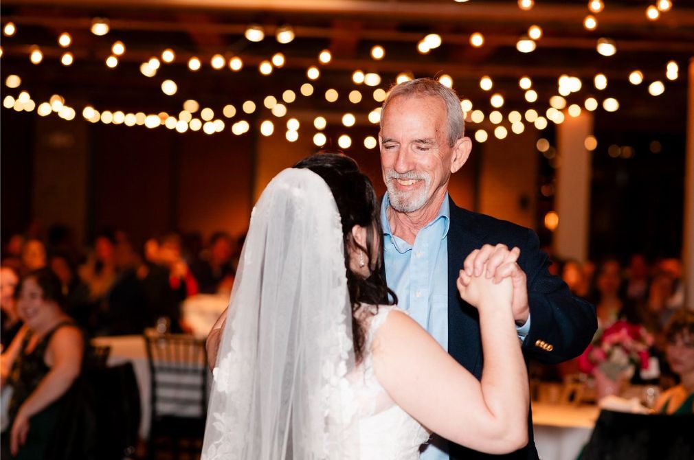 Bride and older man dancing at a reception under warm string lights