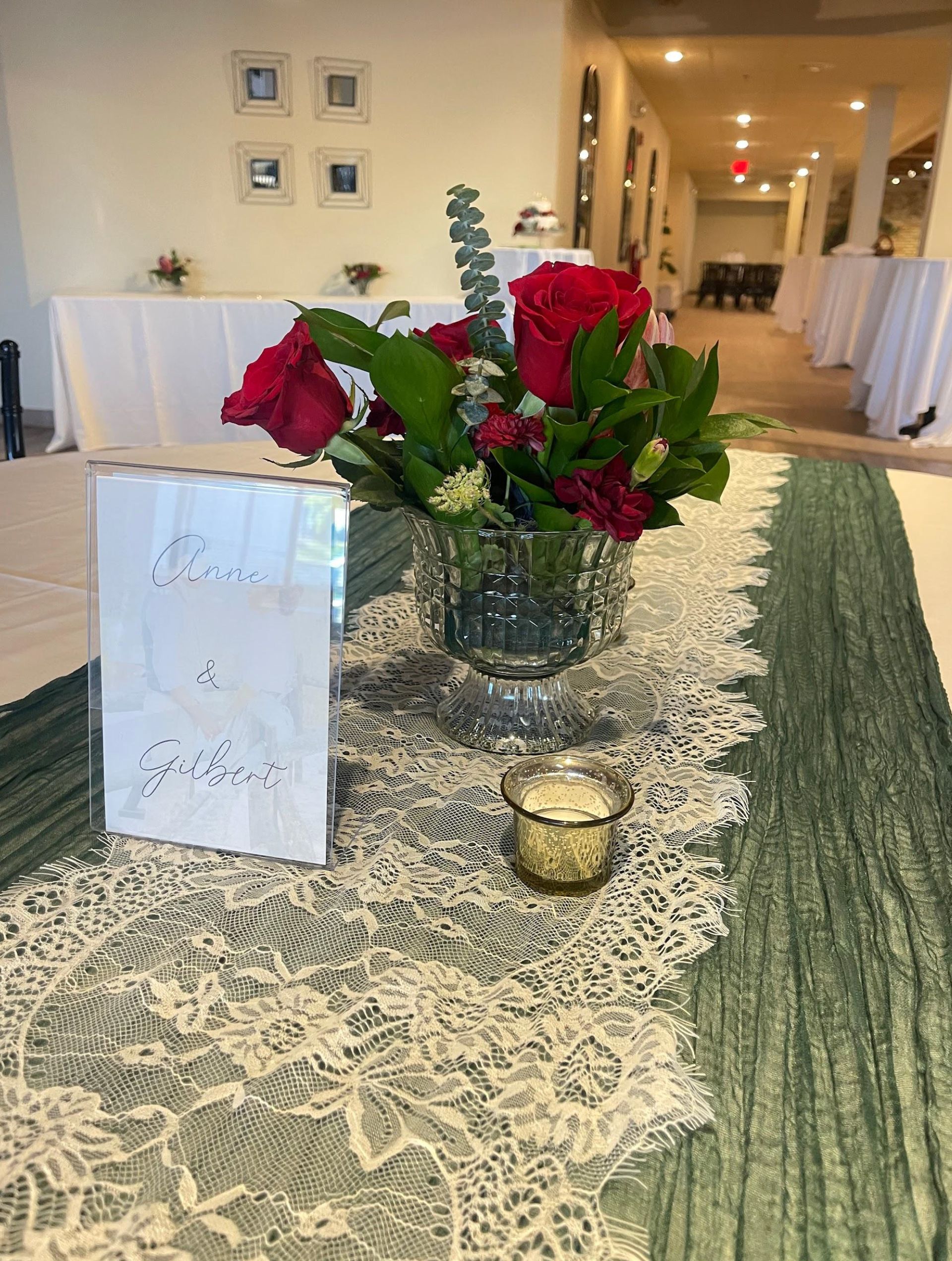 Rose centerpiece on a lace-covered table at a formal indoor event, with a candle and place card.