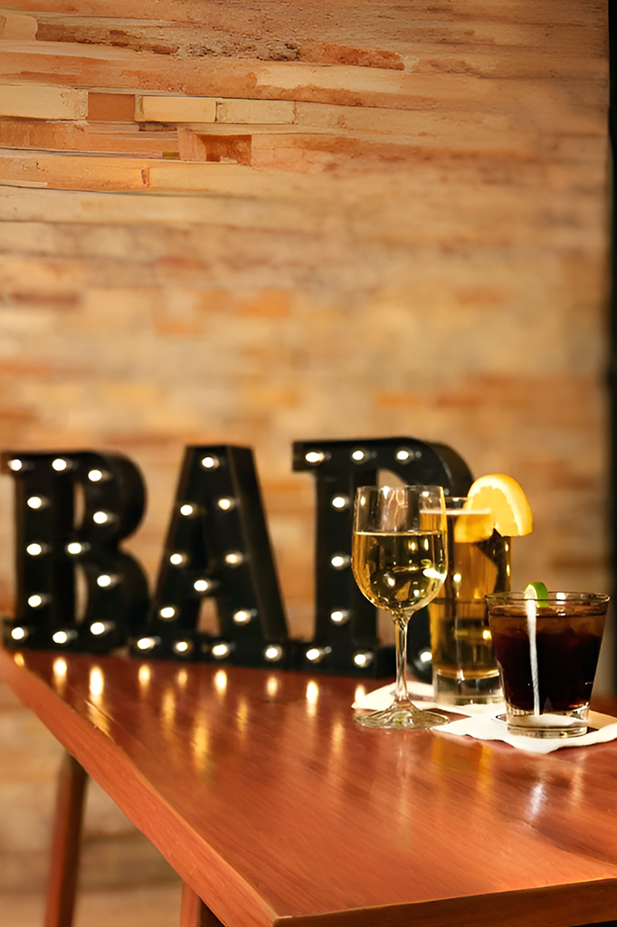 Bar with lit sign, cocktails, and a lemon garnish on a wooden counter