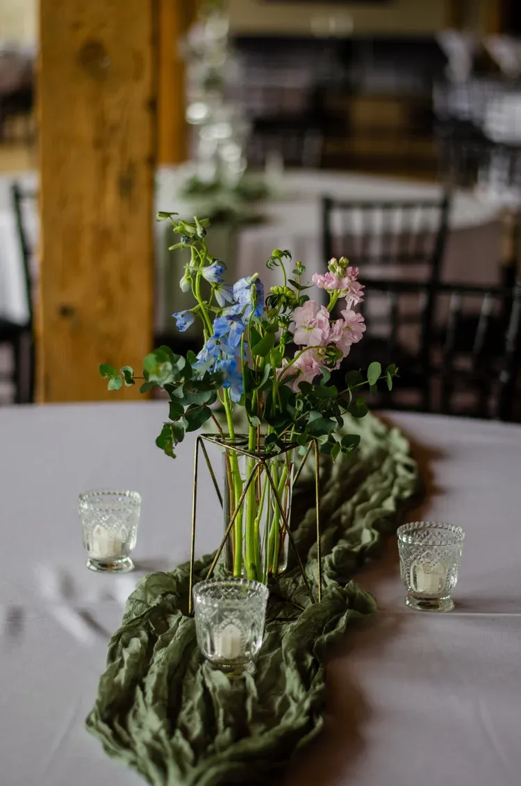 Flower arrangement with blue and pink blooms in a glass vase on a moss-covered table centerpiece