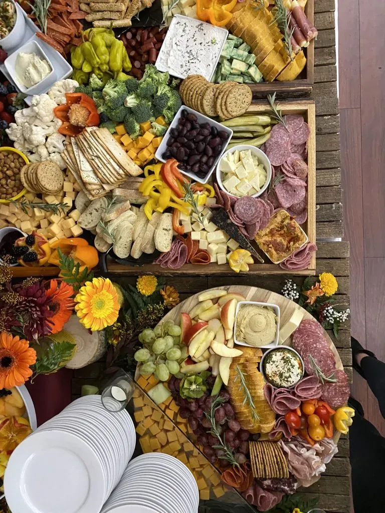 Colorful charcuterie and fruit platters with cheeses, crackers, grapes, and flowers on a rustic table