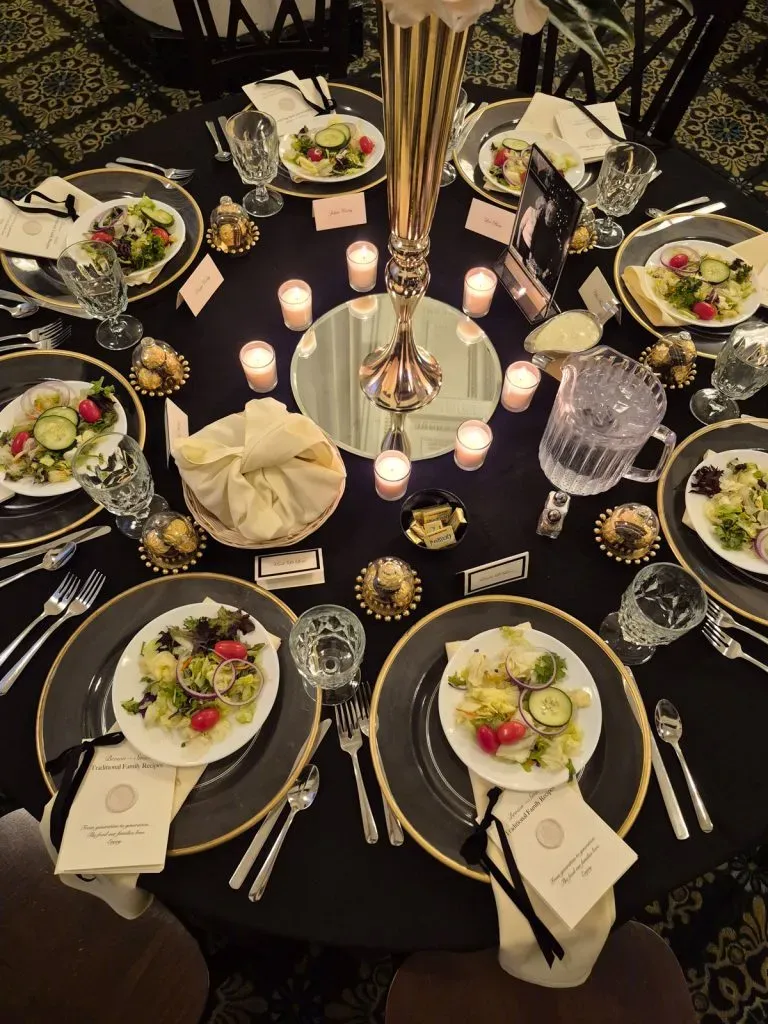 Elegant black-and-gold banquet table set with candles, floral plates, glassware, and folded napkins