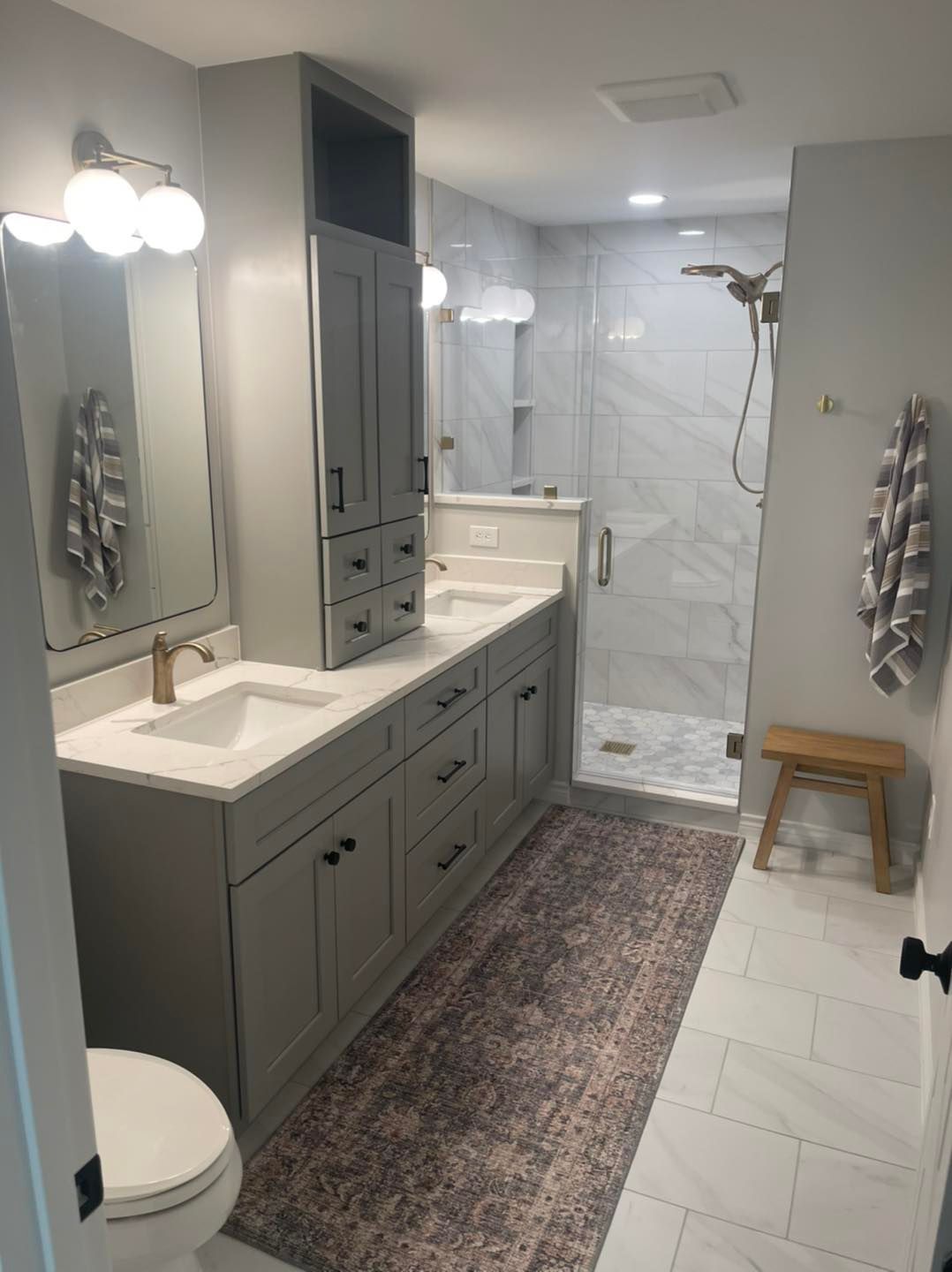 Modern gray-and-white bathroom with double vanity, large mirror, walk-in shower, and patterned rug