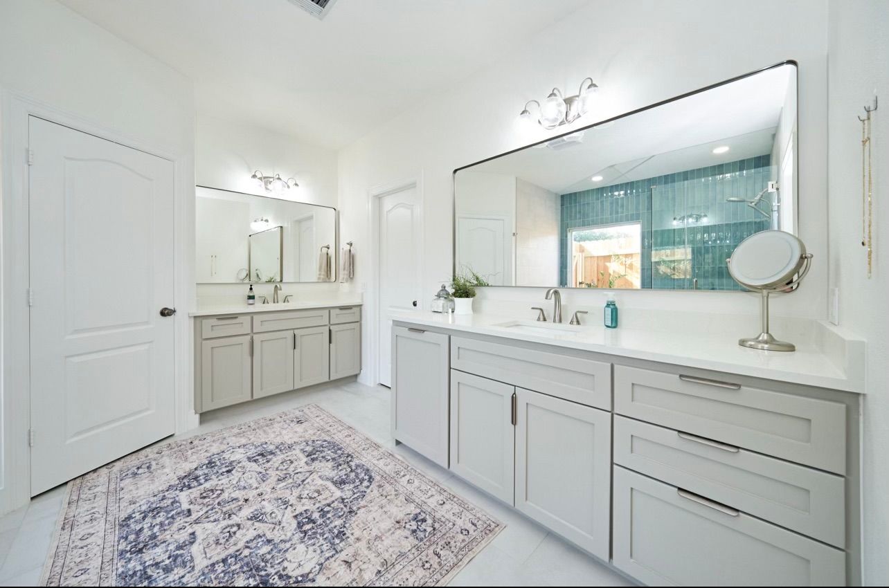 Bright white bathroom with double vanity, large mirror, and patterned rug