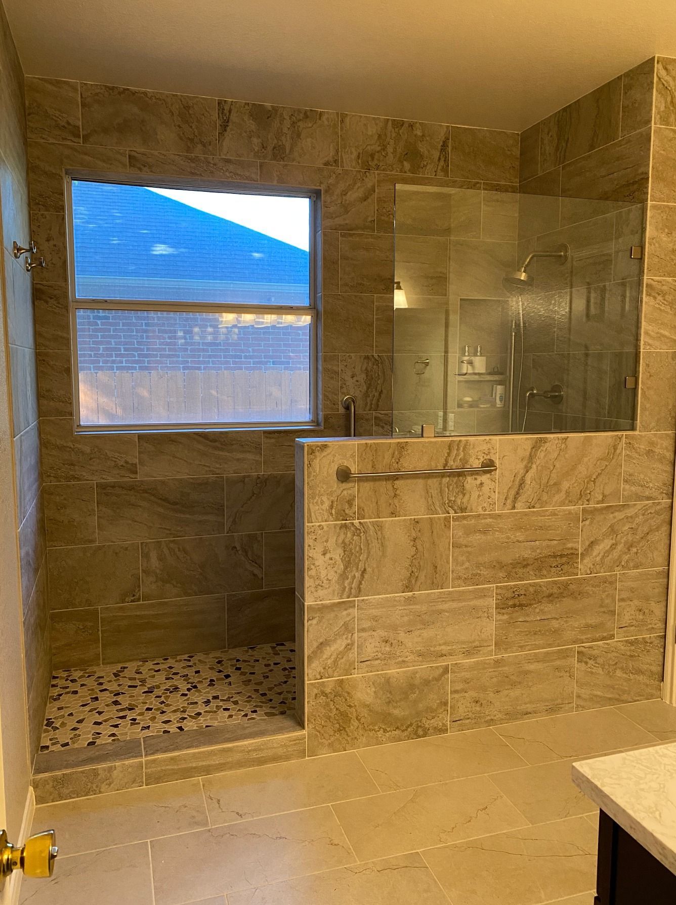 Stone-tiled bathroom with a walk-in shower, glass enclosure, and a window overlooking a blue mountain view