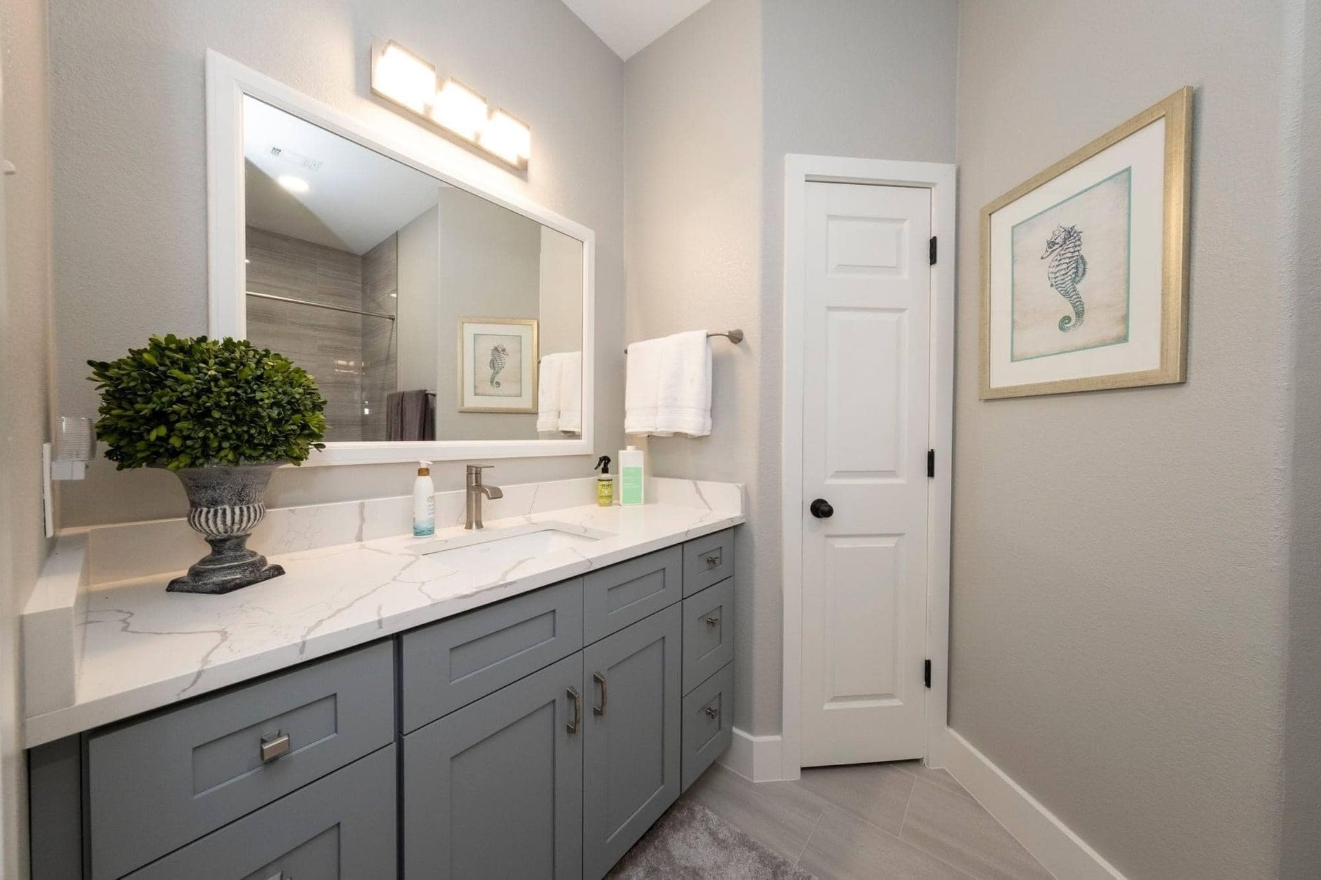 Modern bathroom with blue vanity, large mirror, white walls, and framed artwork
