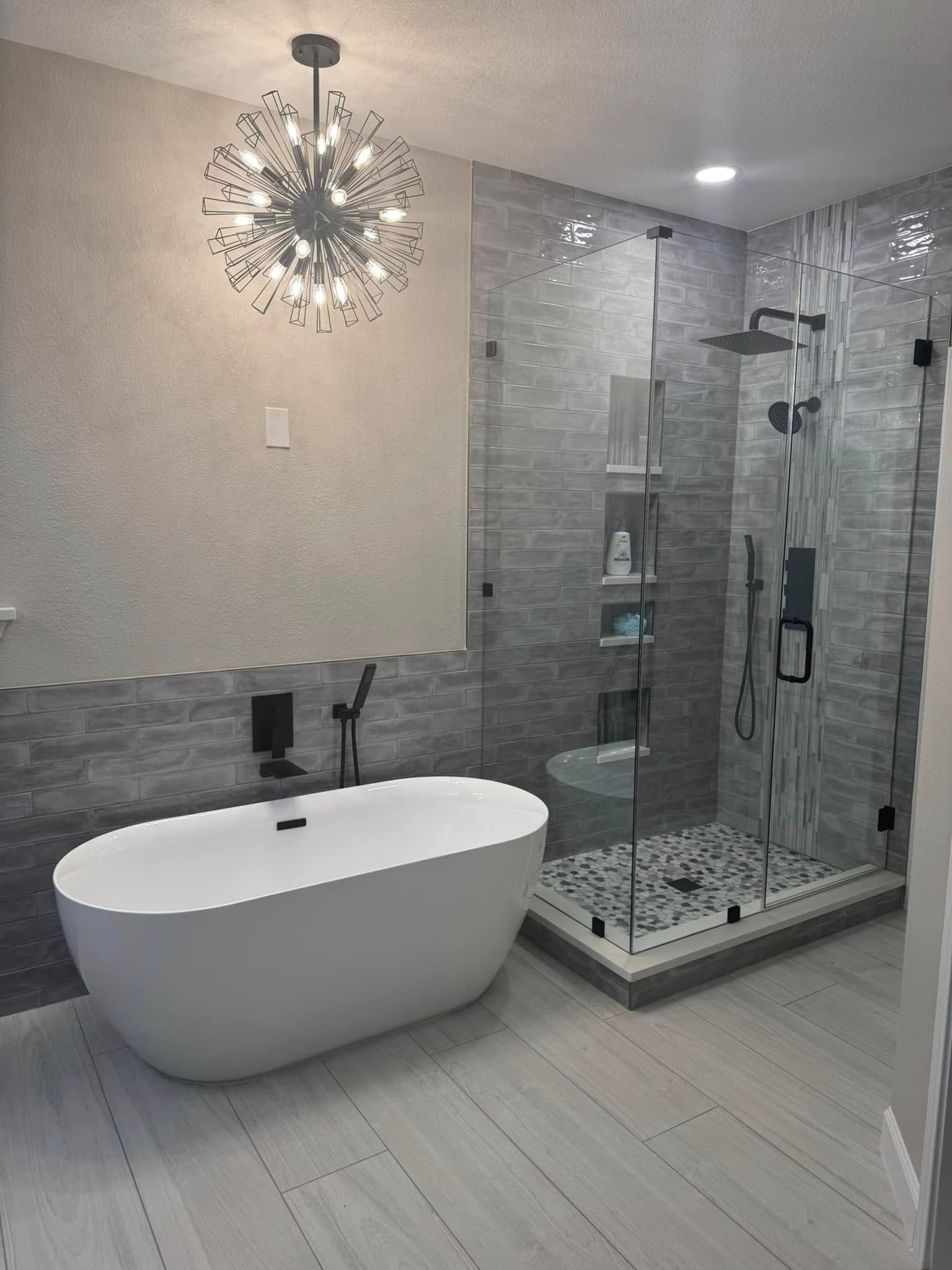 Modern bathroom with freestanding tub, glass shower, gray tile, and starburst light fixture