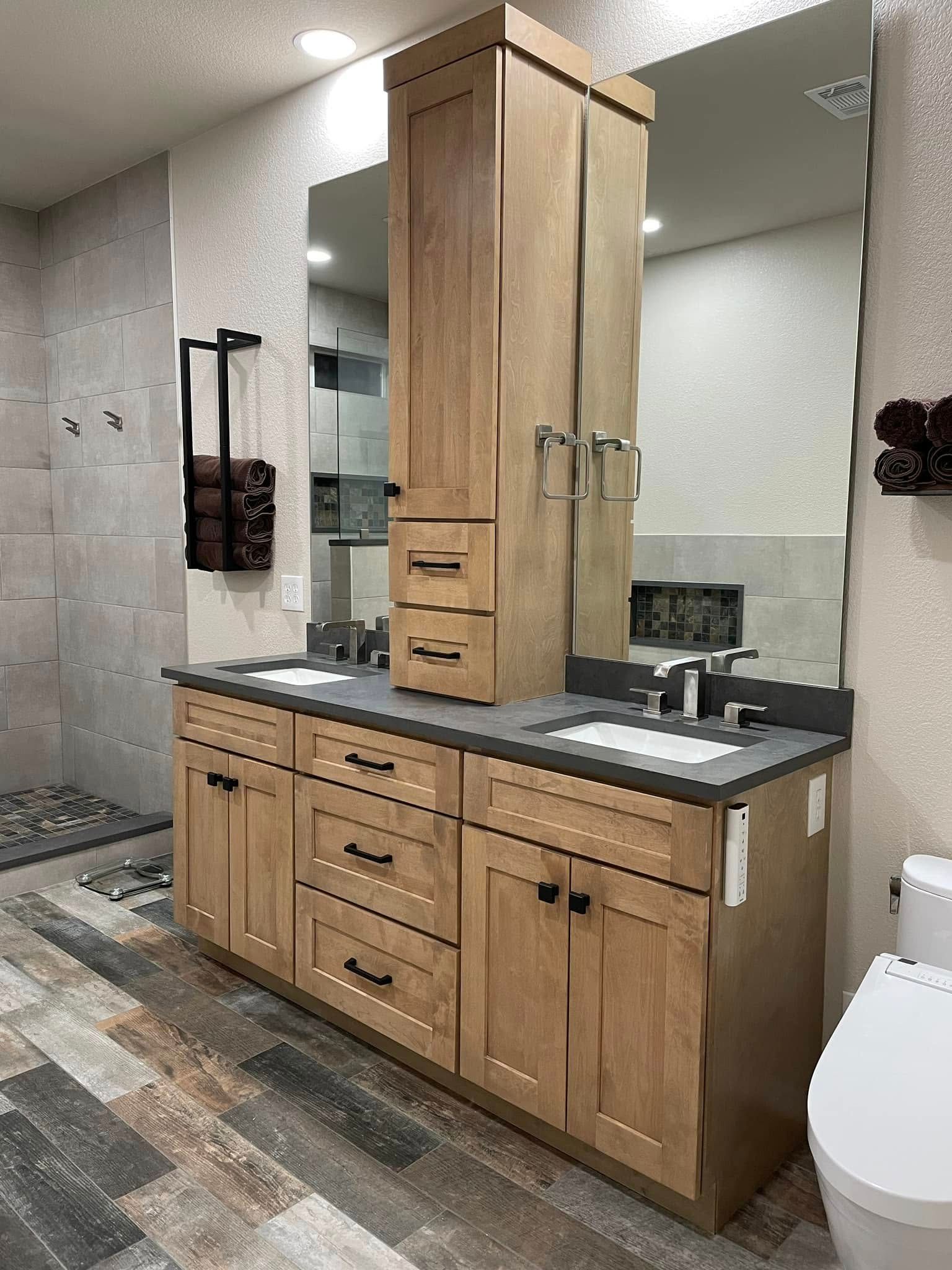 Modern bathroom vanity with wood cabinets, gray countertop, large mirrors, and patterned tile flooring.