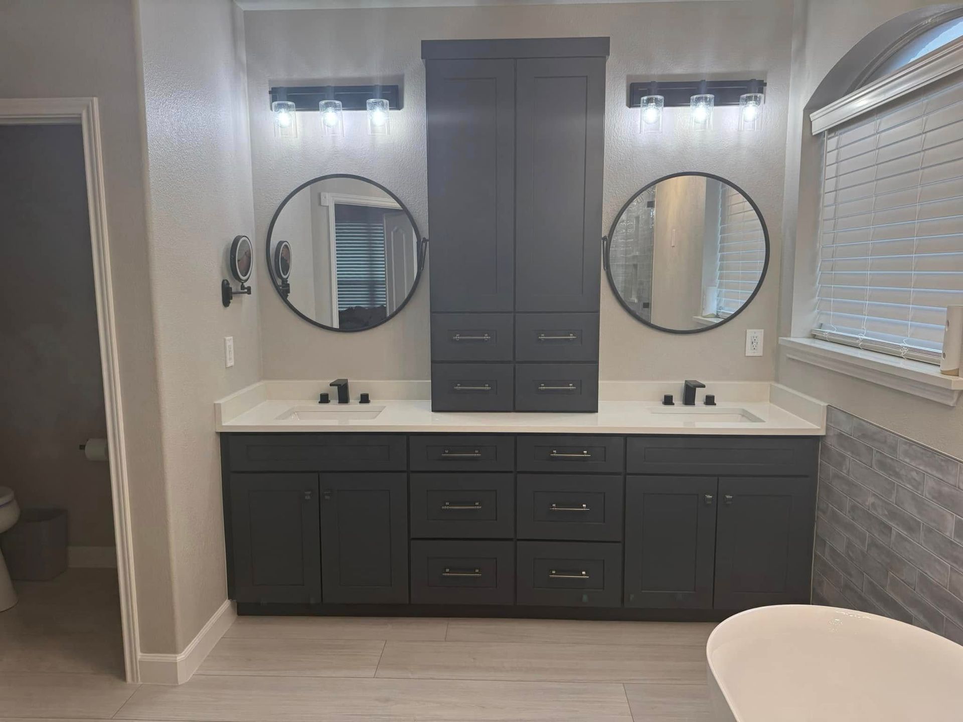 Modern bathroom vanity with double sinks, round mirrors, dark cabinets, and gray tile wall.