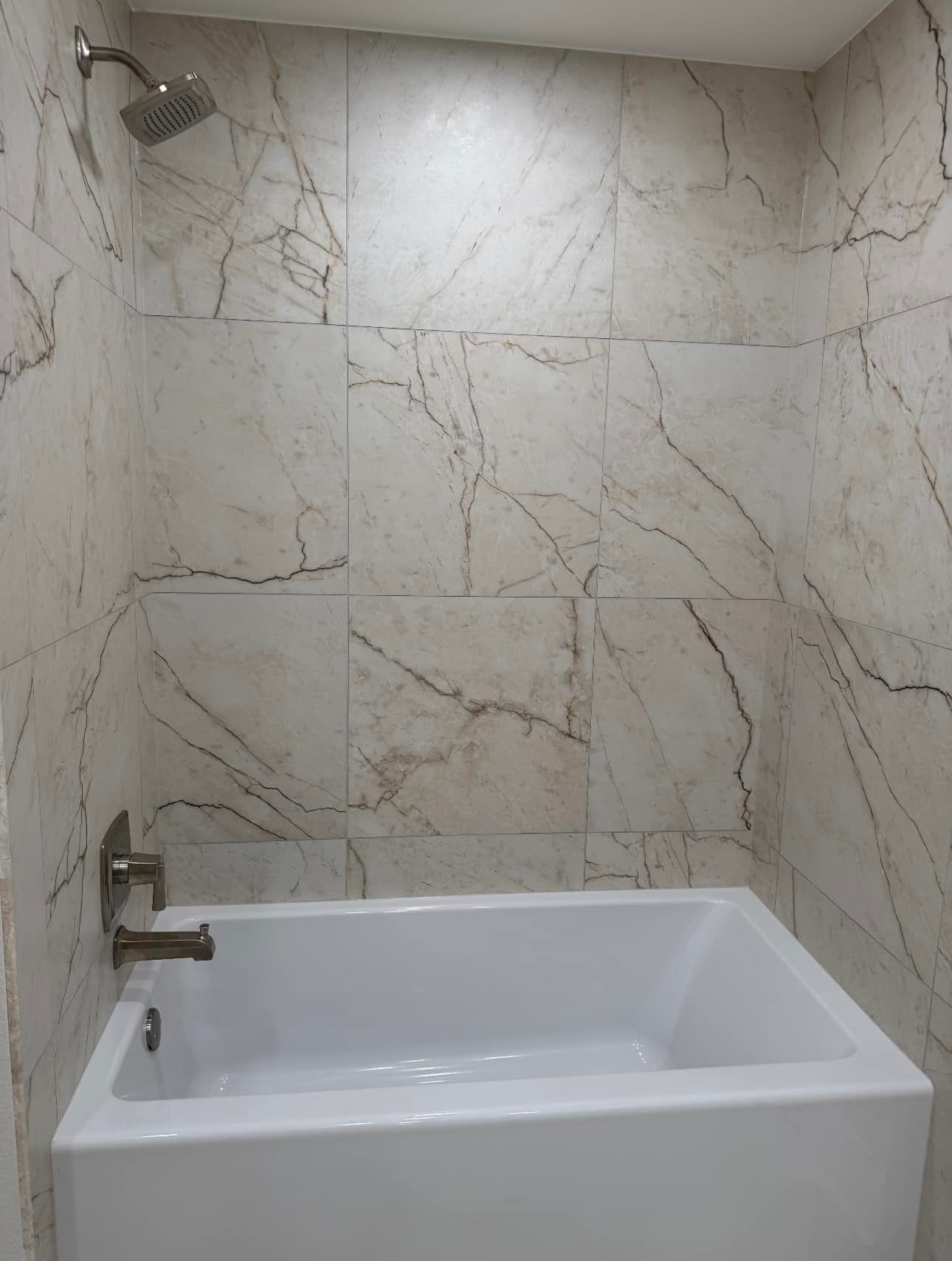 Modern bathroom shower-bathtub with white marble-look tile walls and a chrome showerhead and faucet.