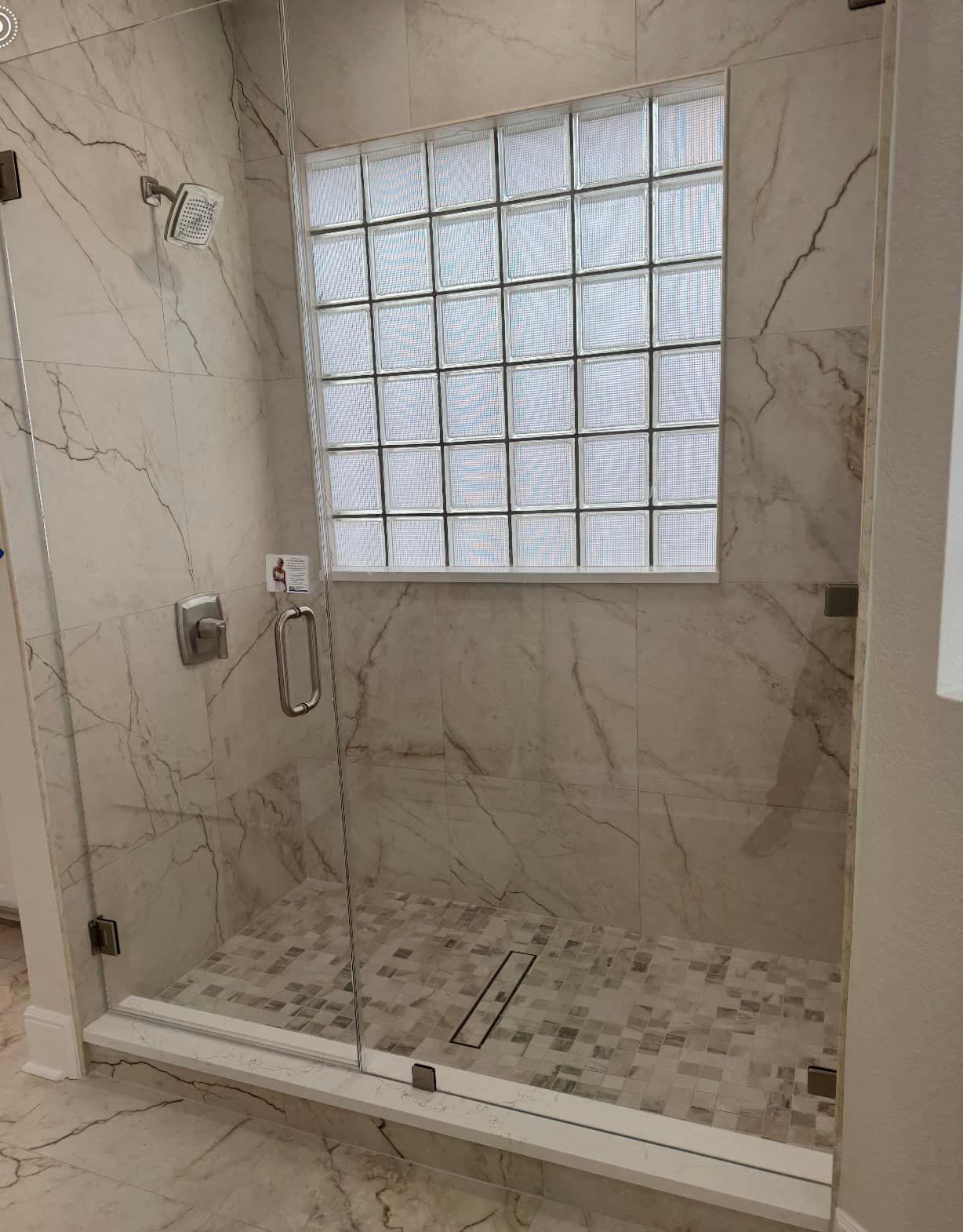 Glass-enclosed shower with marble tile walls, pebble floor, and a frosted glass block window