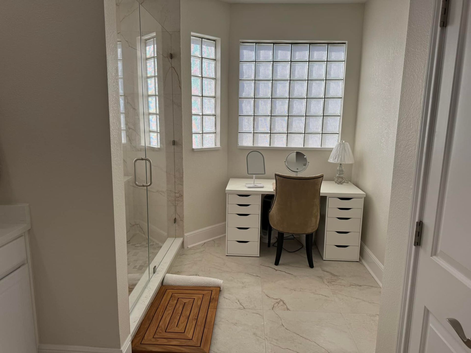 Small home office with white desks, a chair, and large windows in a bright room