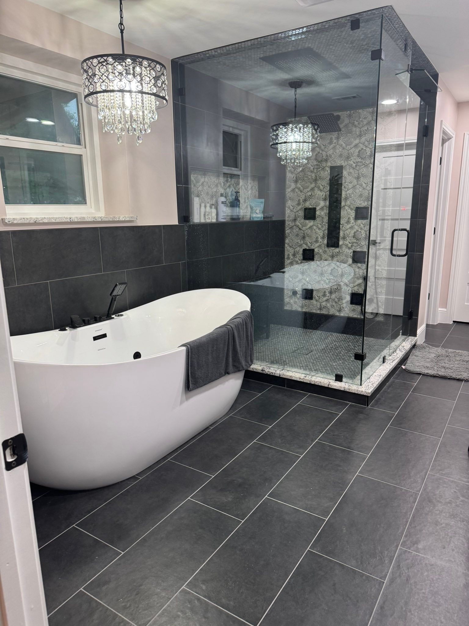 Modern bathroom with freestanding tub, glass shower, black tile floor, and chandelier lighting