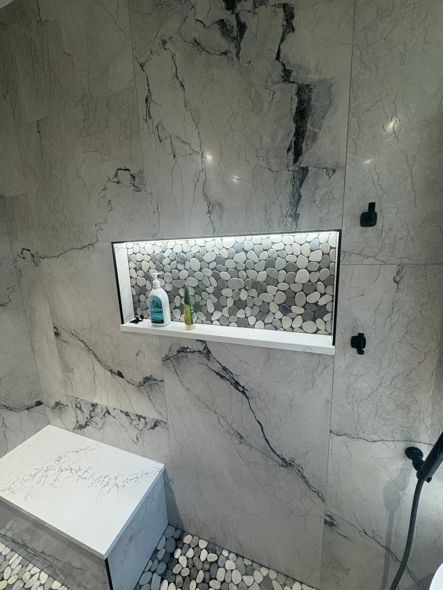 Small bathroom with marble-pattern tile wall, built-in shelf niche, toilet, and handheld shower fixture.