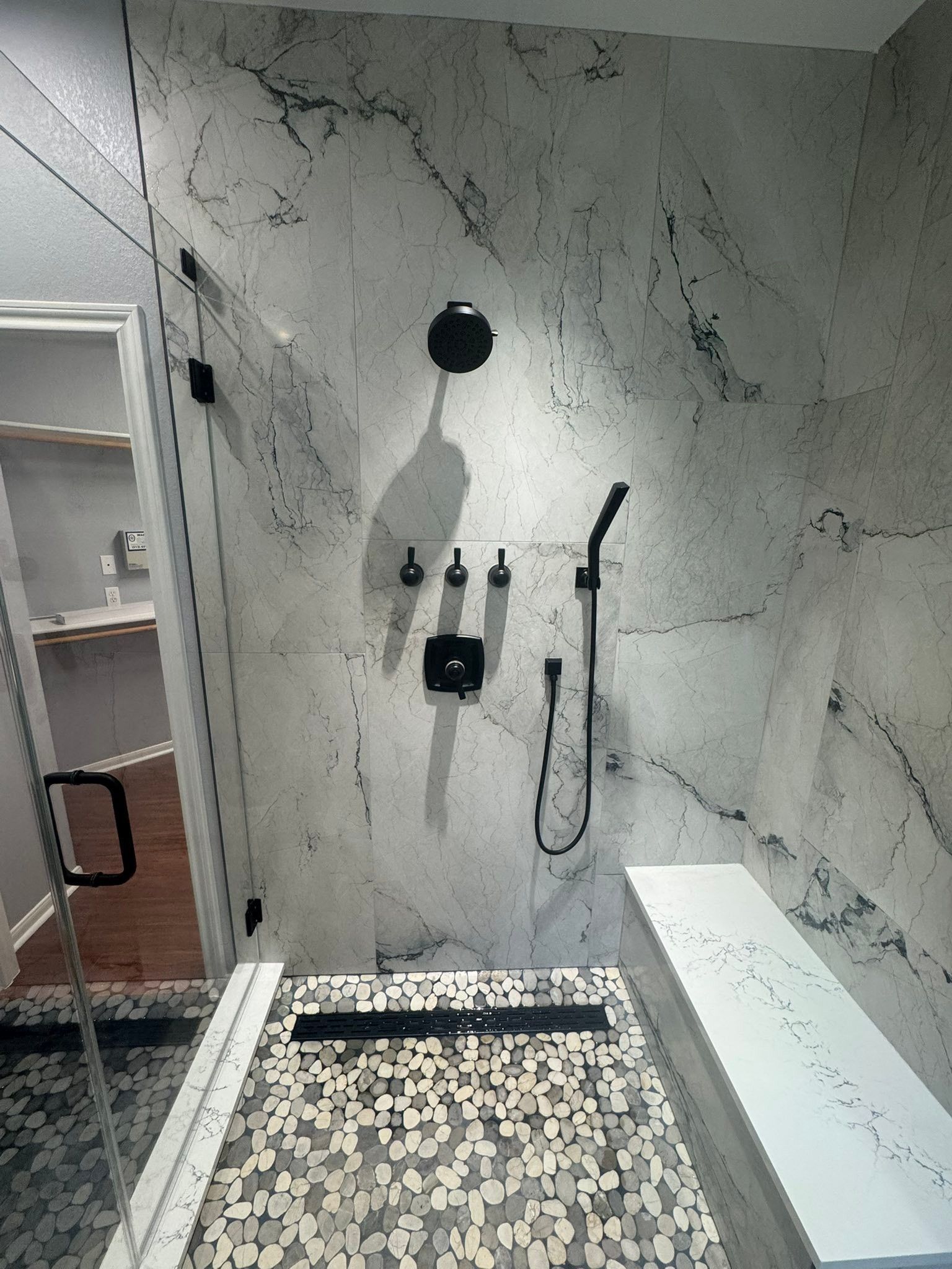 Modern shower with marble-look tile, wall-mounted fixtures, and a pebble-stone floor.