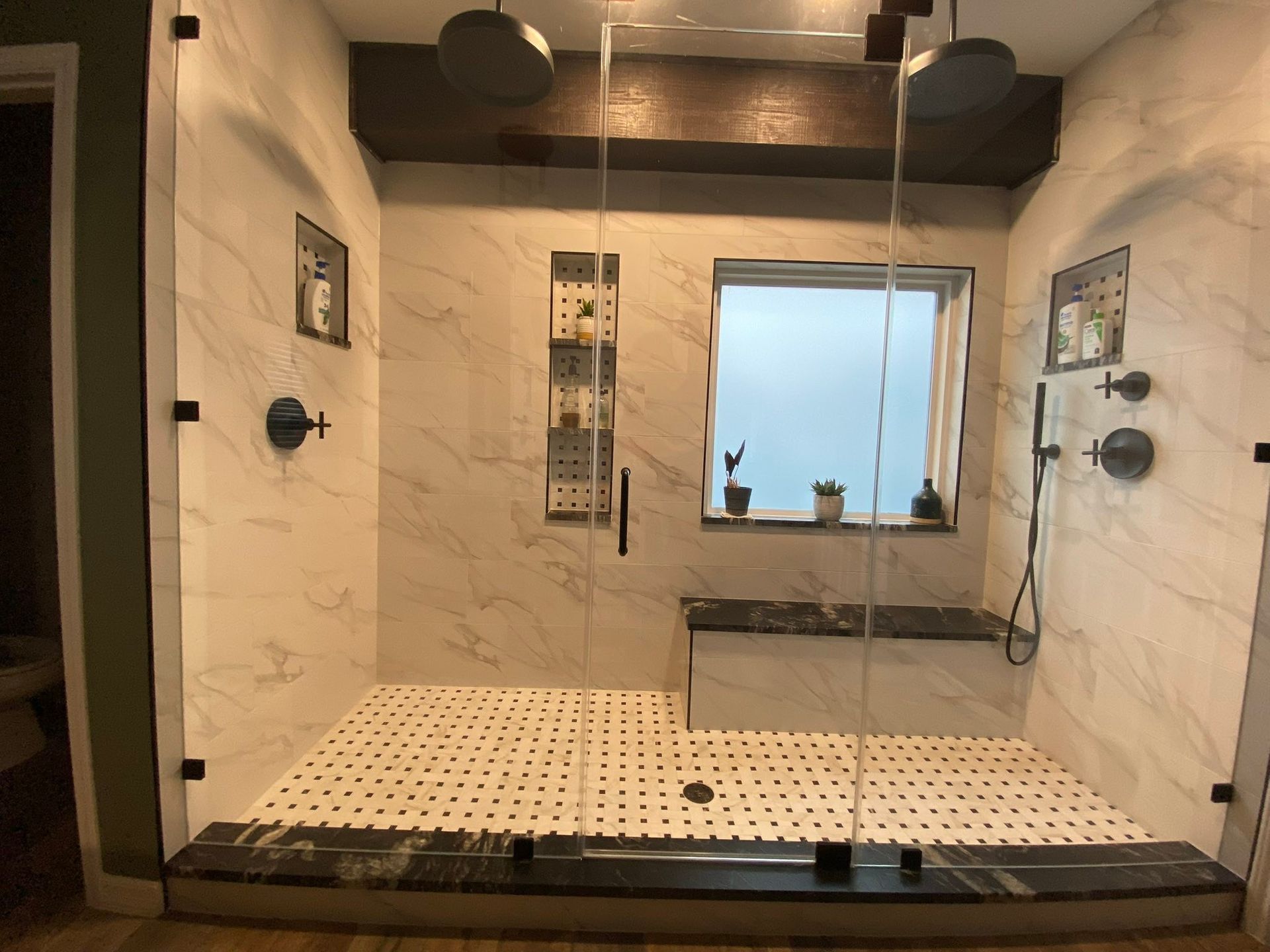Modern shower with marble walls, black fixtures, glass door, and pebble-tile floor.