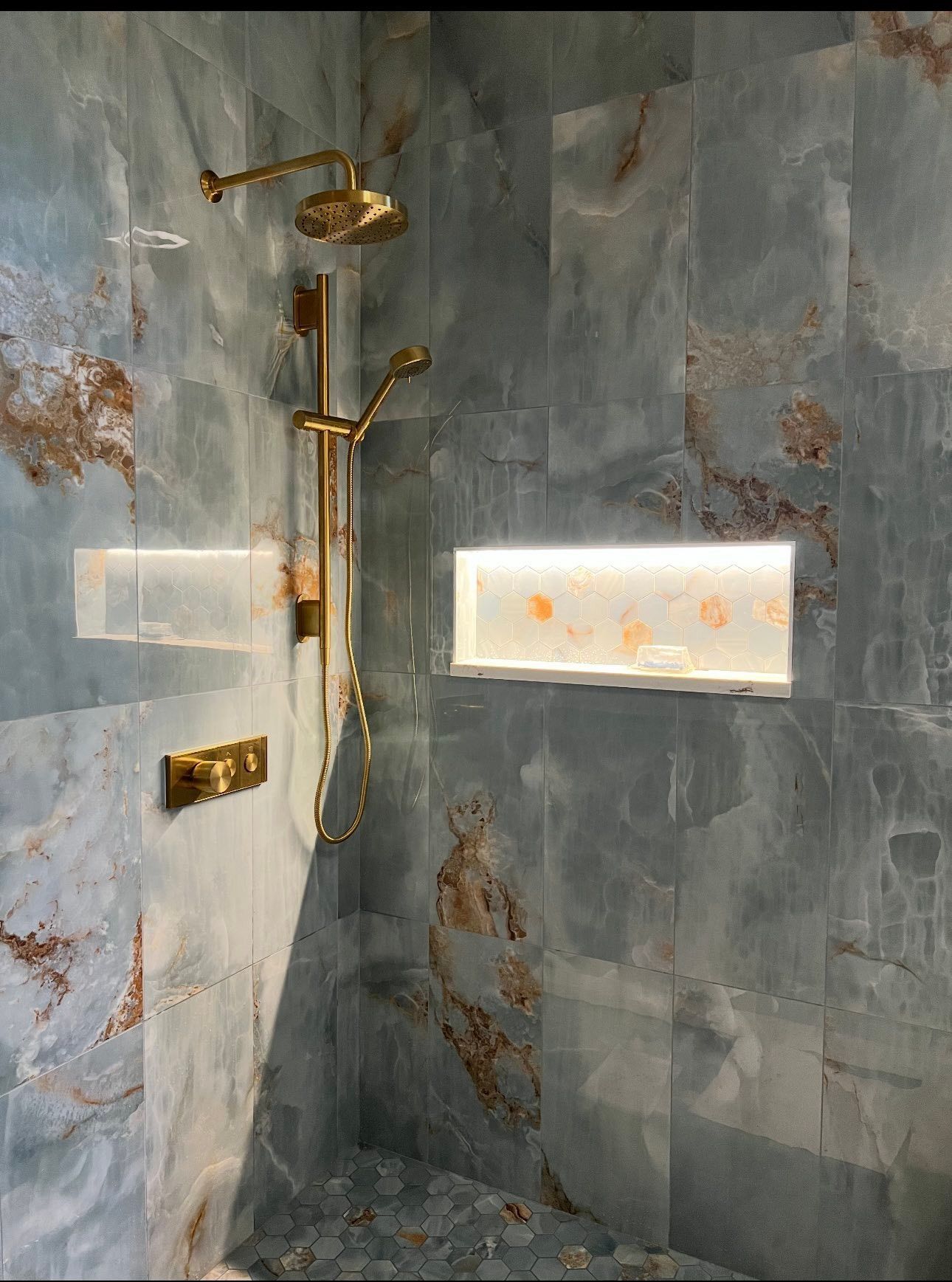 Modern shower with gray stone tile, gold fixtures, and a small frosted window.