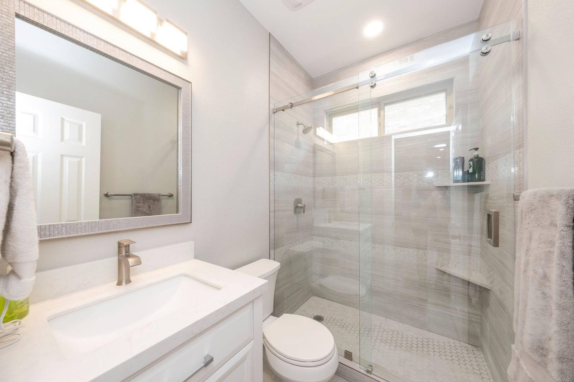 Bright modern bathroom with white vanity, mirror, toilet, and glass-enclosed shower