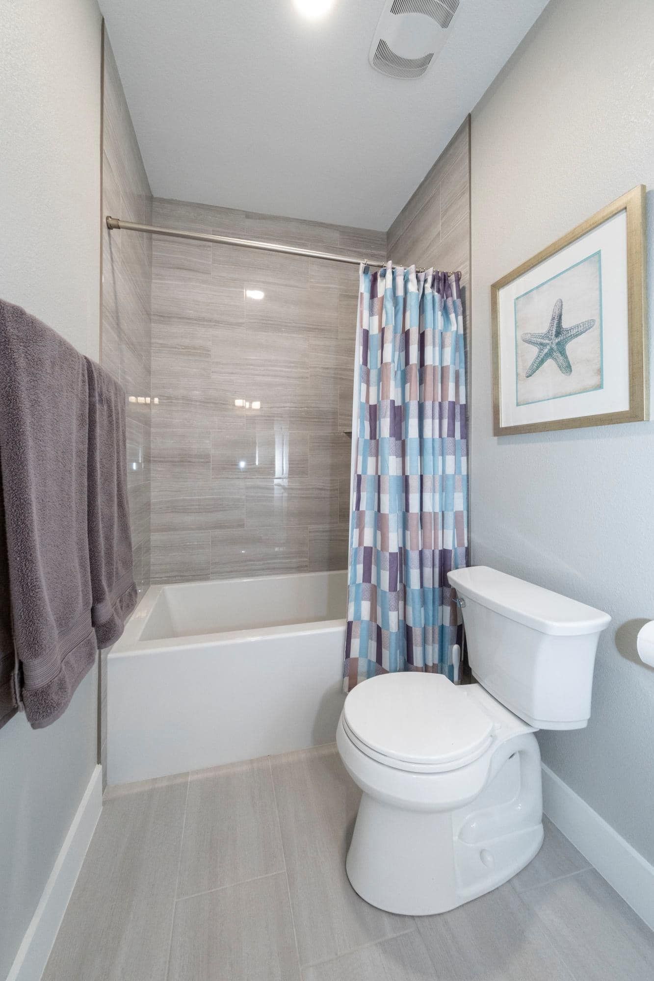 Compact bathroom with white toilet, bathtub, and shower curtain in a narrow gray-toned space