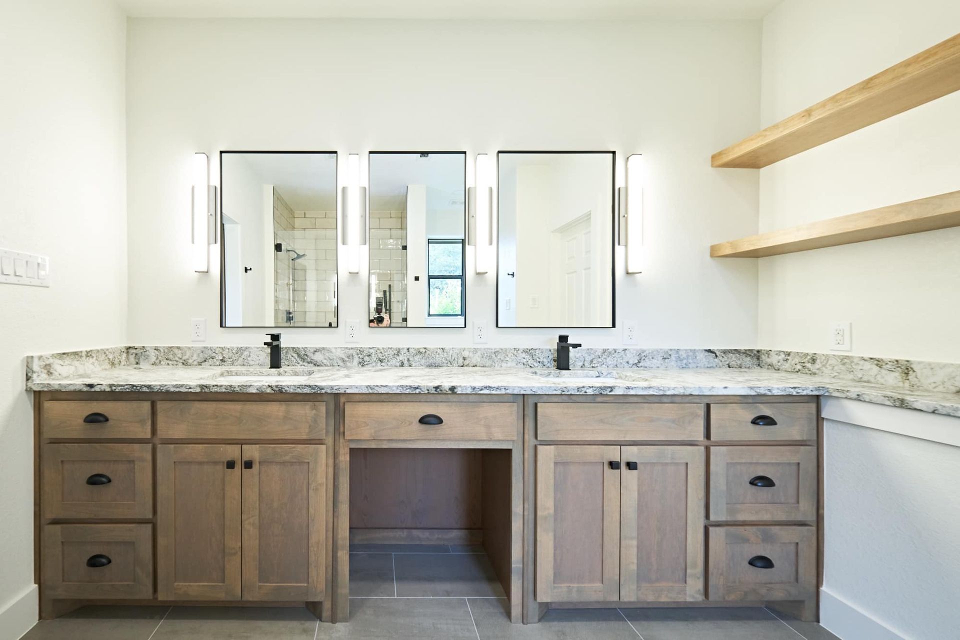 Spacious bathroom vanity with double sinks, three mirrors, wood cabinets, and granite countertop.