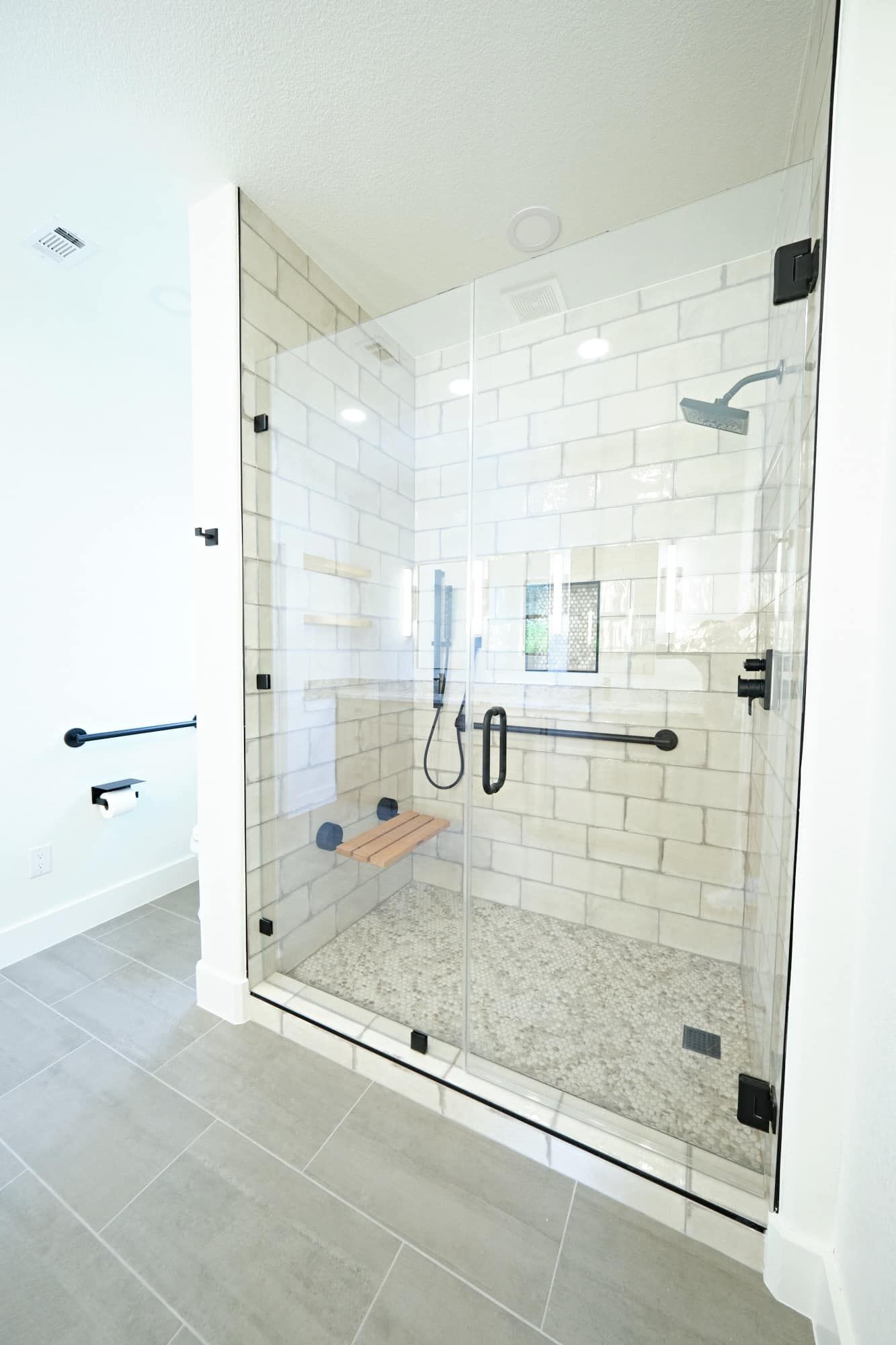 Glass walk-in shower with white subway tile and gray floor in a bright bathroom