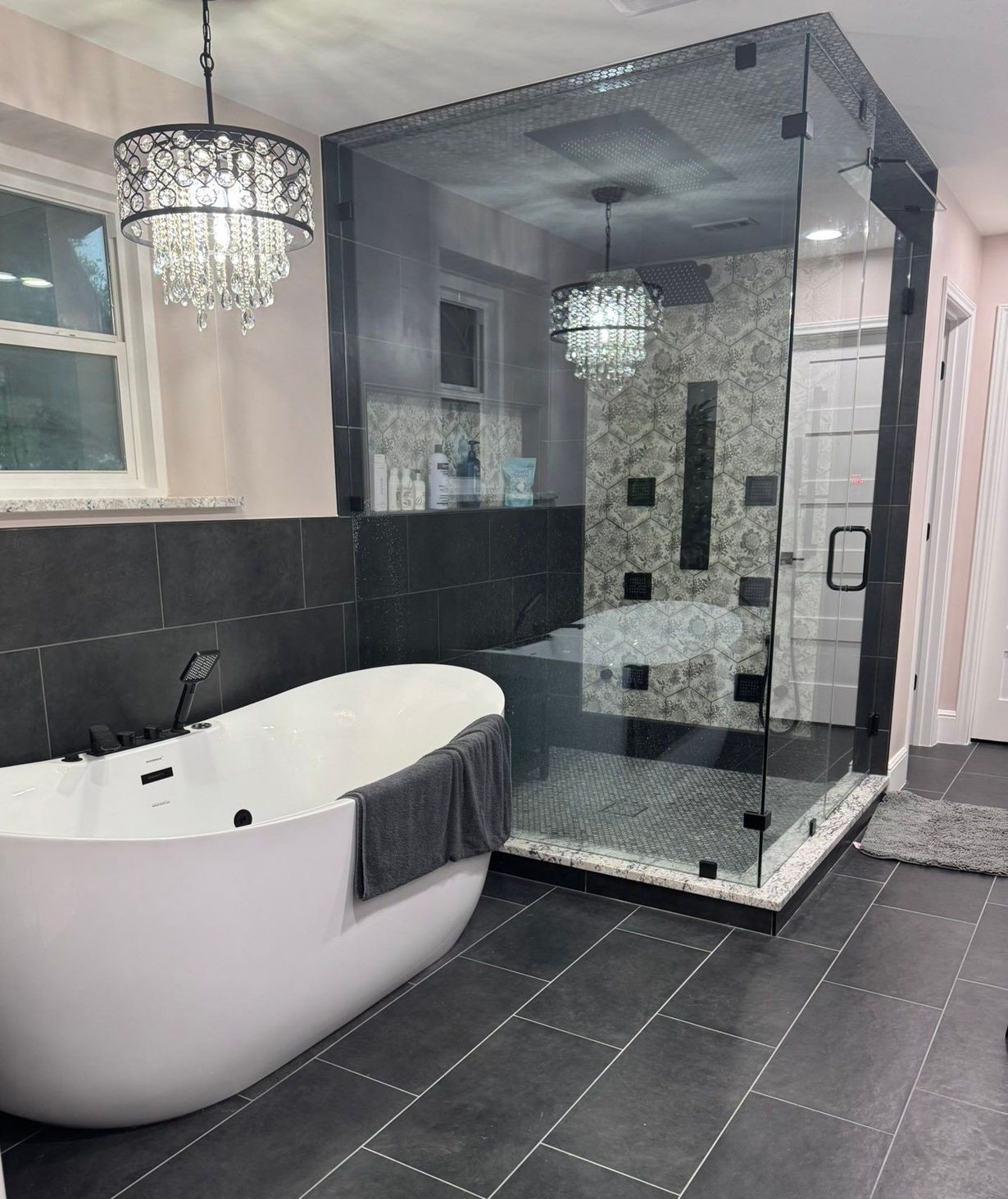 Modern bathroom with freestanding tub, glass shower, black tile, and chandelier lighting