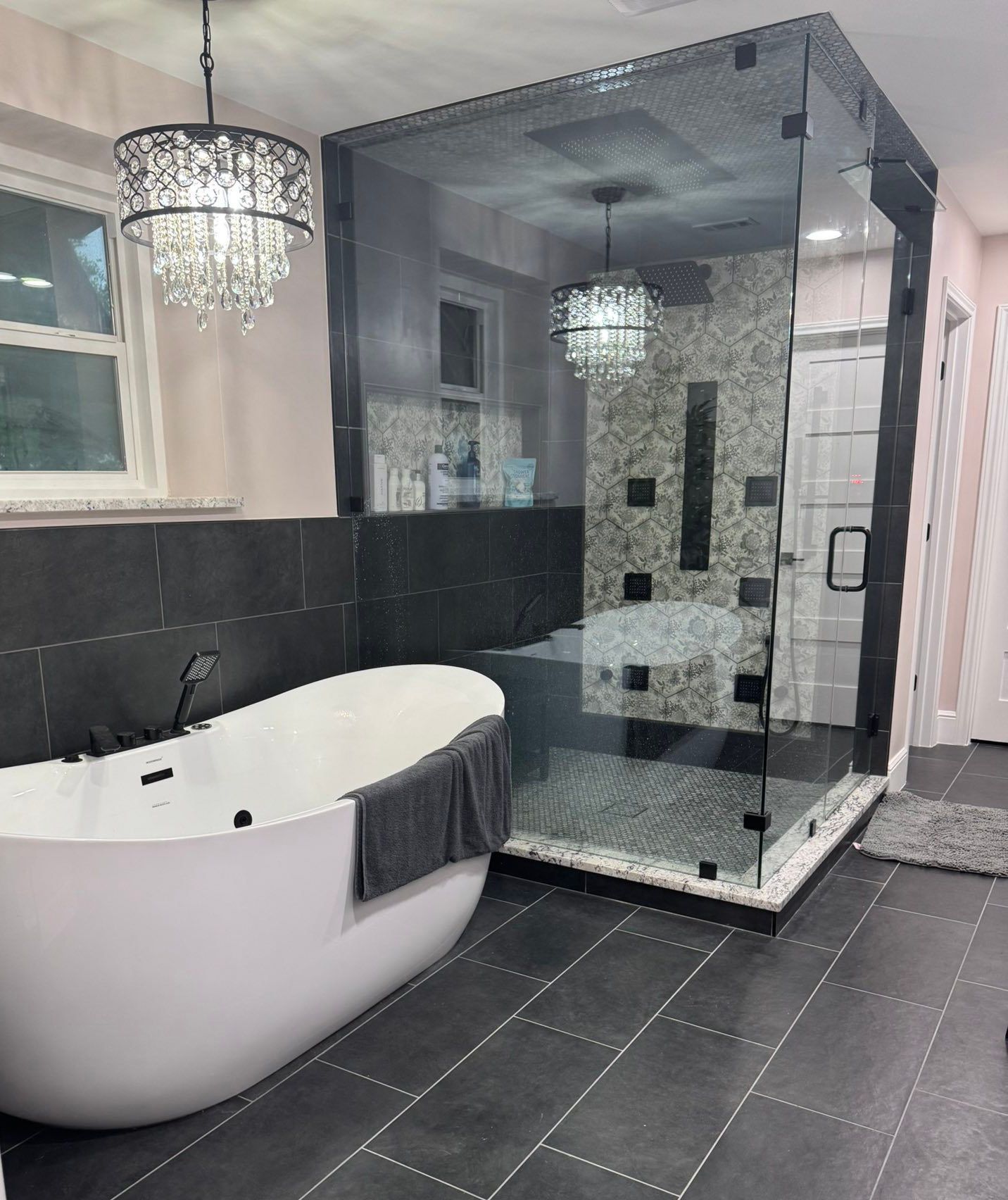 Modern bathroom with freestanding tub, glass shower, black tile, and chandelier lighting