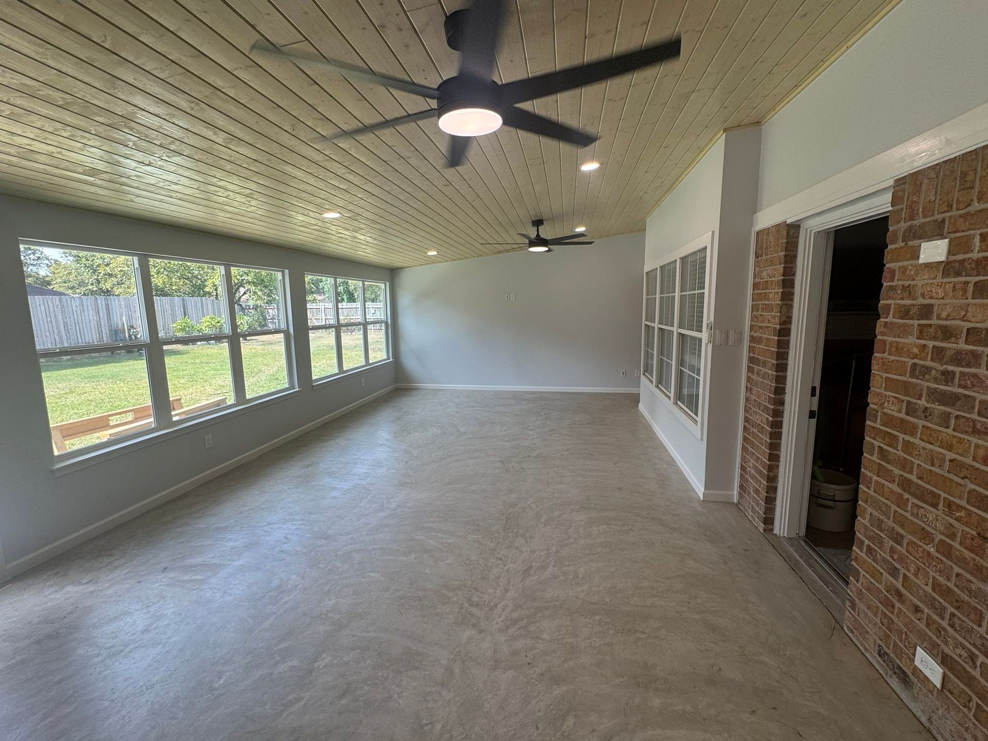 Empty enclosed porch with ceiling fans, large windows, and brick walls