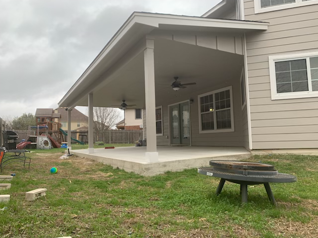 Covered patio on a gray house with a grassy yard and fire pit in the foreground