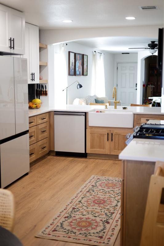 Bright modern kitchen with white cabinets, wood flooring, island, and a runner rug leading to a living area