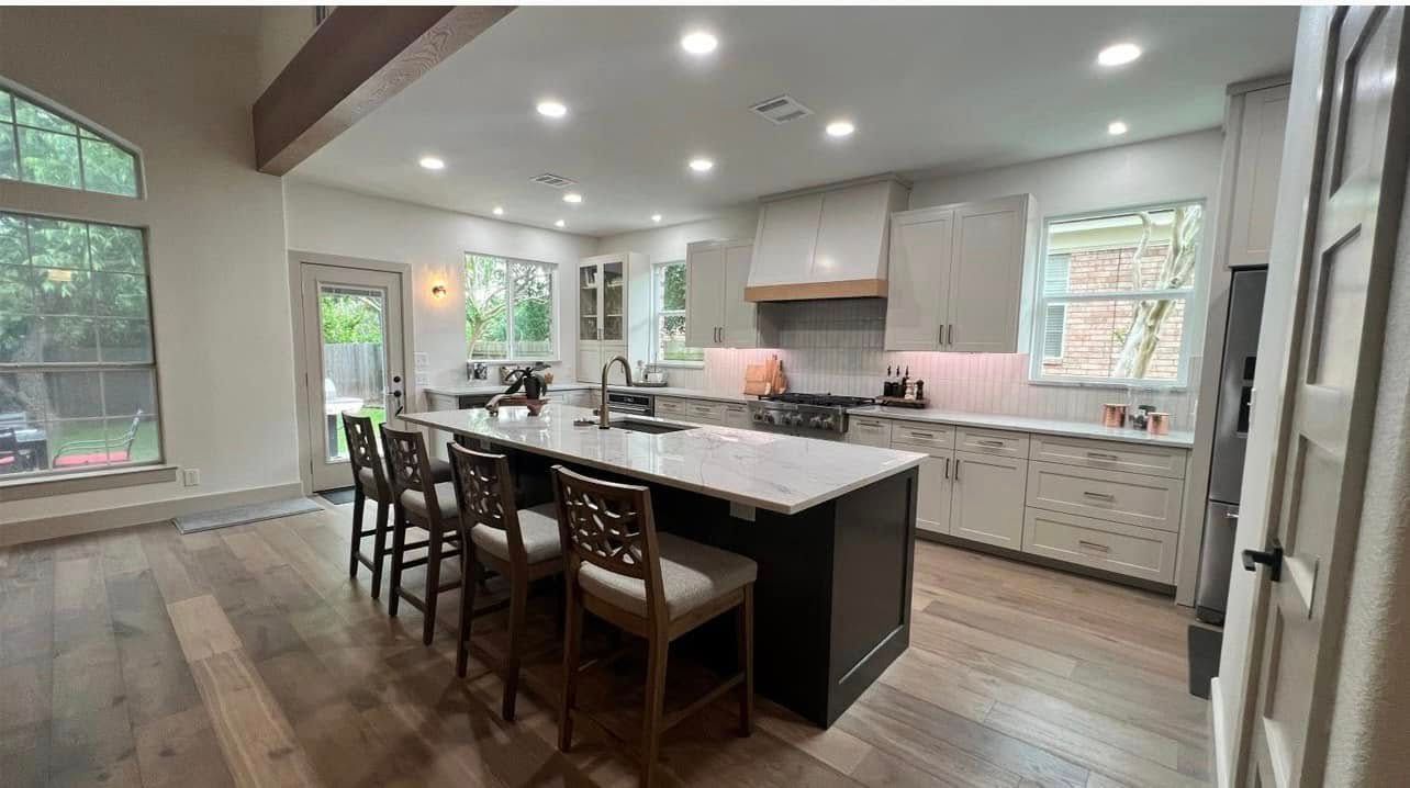 Bright modern kitchen with white cabinets, large island, bar stools, and wood floors, viewed from a doorway