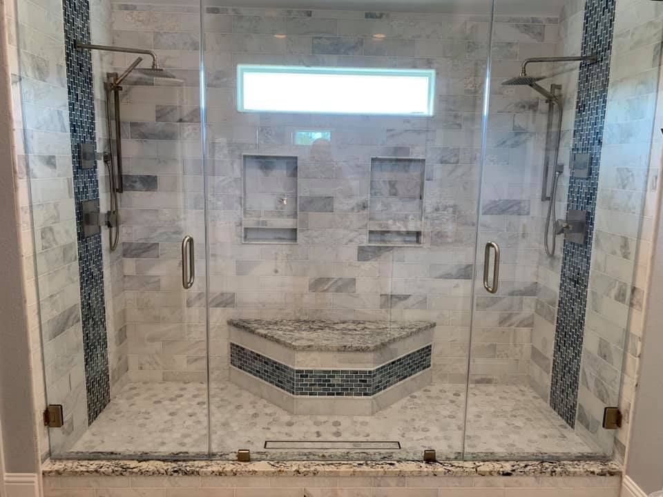 Glass walk-in shower with marble tile walls, dual niches, and a built-in corner bench