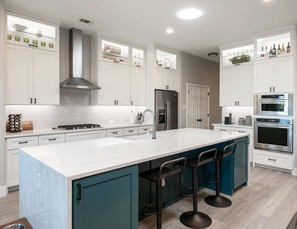 Modern white kitchen with large island, teal cabinets, stainless appliances, and pendant stools