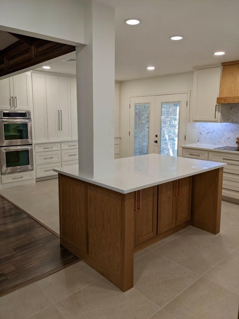 Modern kitchen with white island, wood cabinets, tile floor, and double glass doors