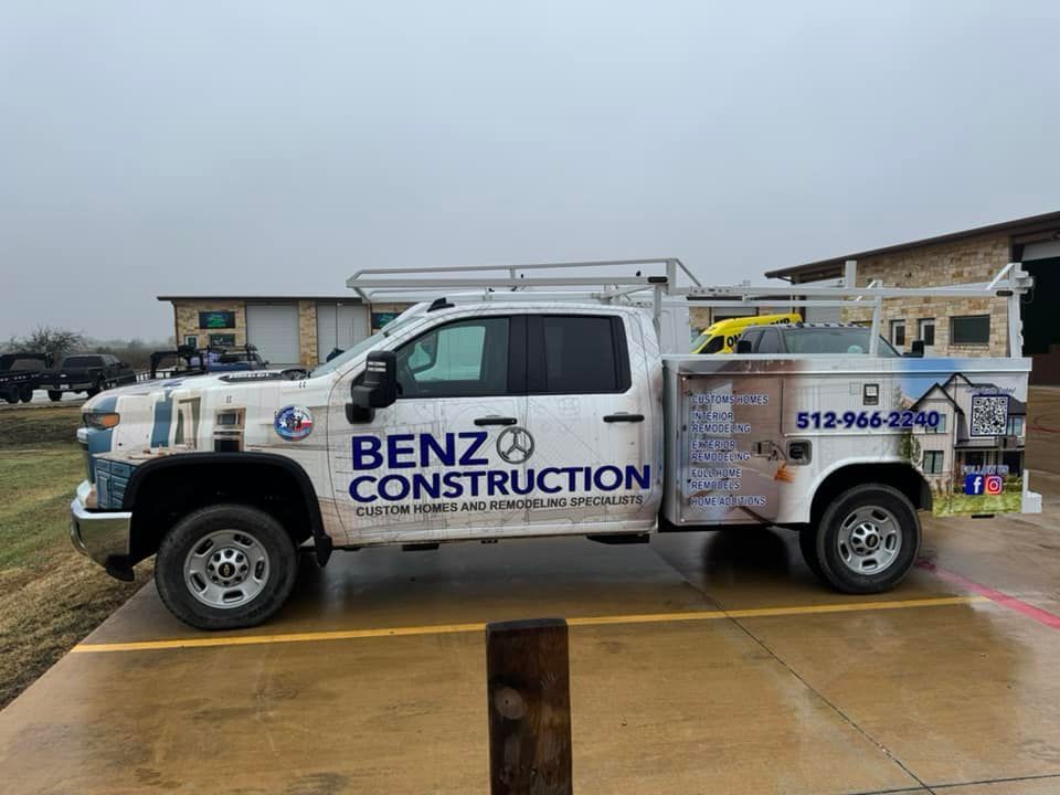 White BENZ Construction work truck parked on wet pavement, side view with company logo and phone number.