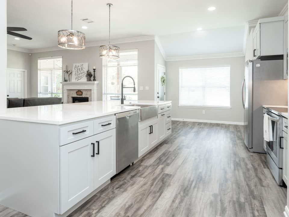 Bright modern kitchen with white cabinets, island, pendant lights, and gray wood-look floors