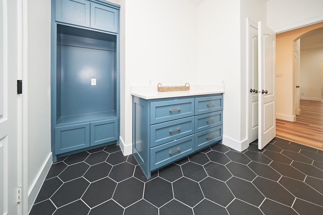 Blue built-in closet and dresser in a bright hallway with black hexagon tile flooring.