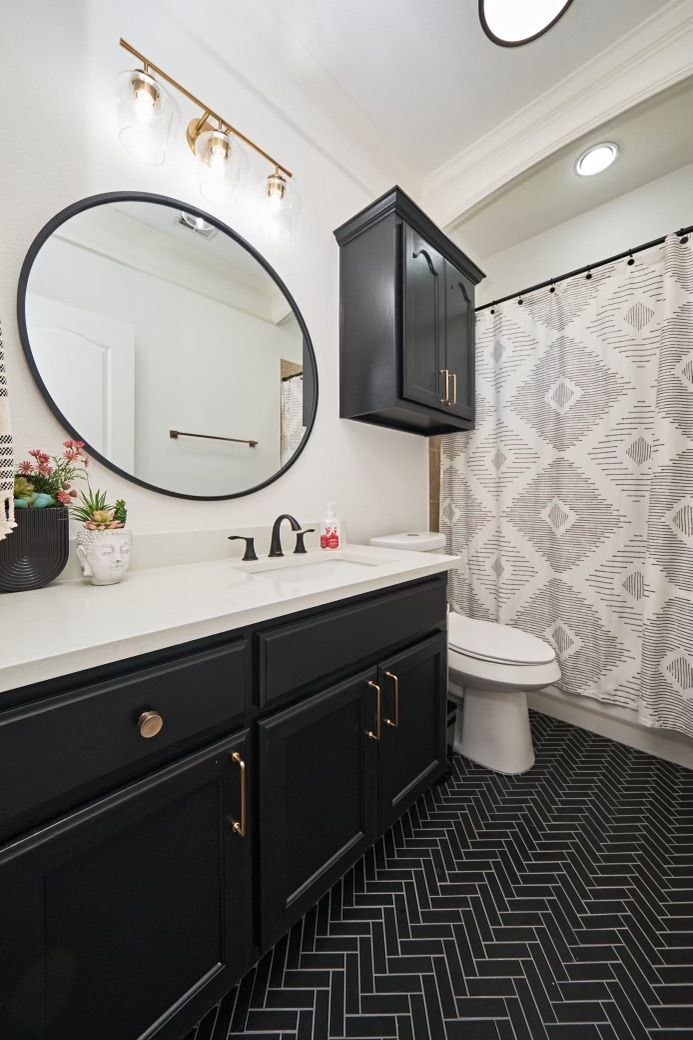 Modern black-and-white bathroom with round mirror, black vanity, and patterned shower curtain