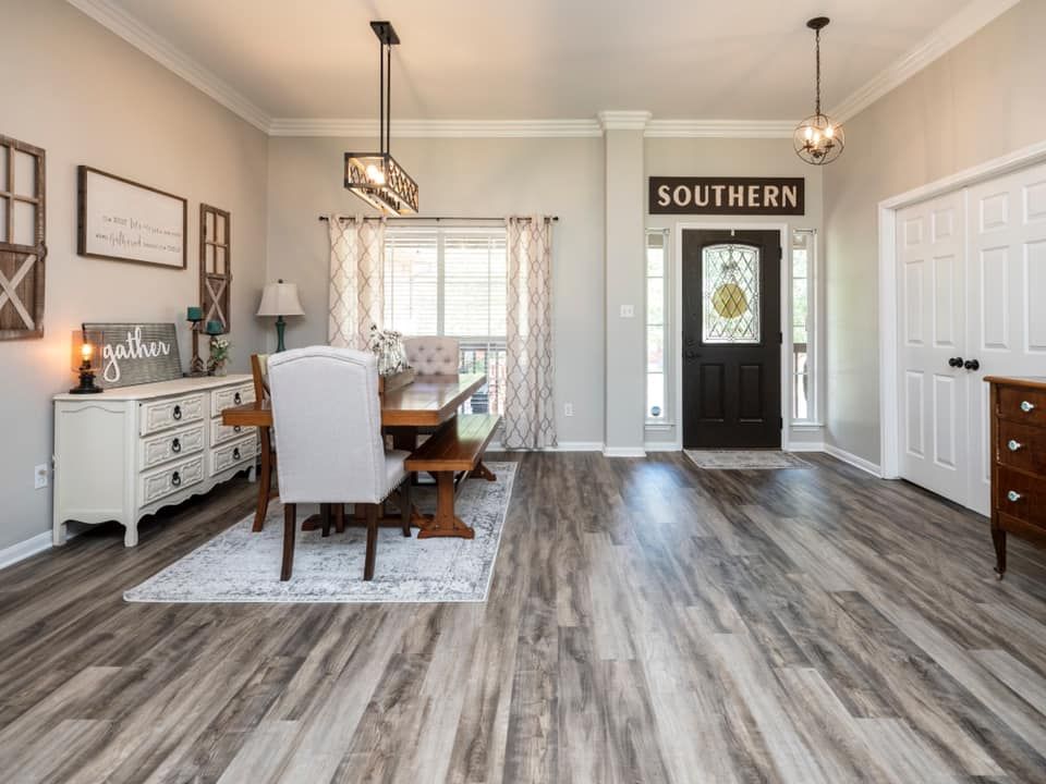 Bright open dining room with wood floors, table, chairs, and a black front door labeled “SOUTHERN”